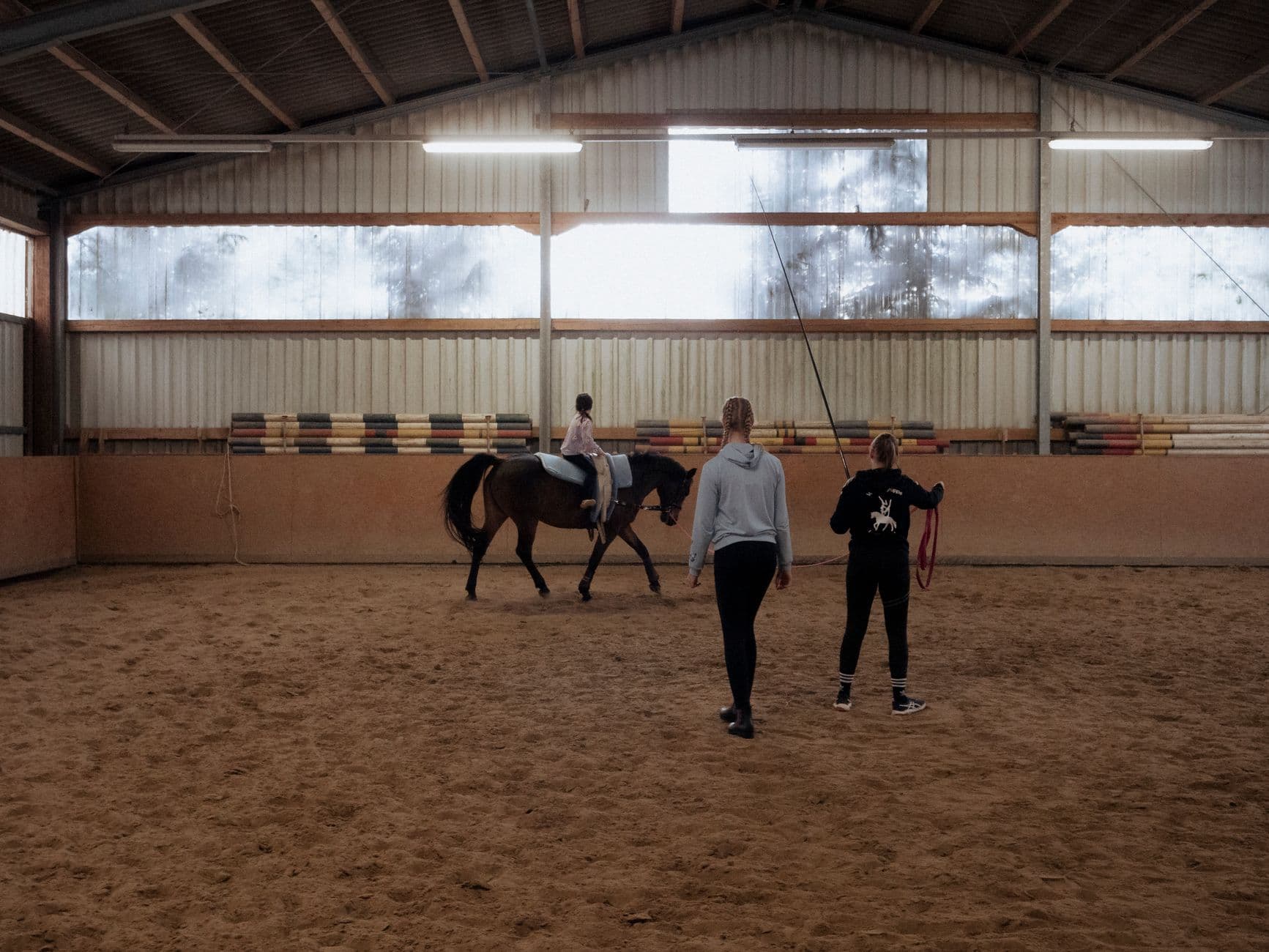 A young girl receives horse riding lessons indoors under guidance.