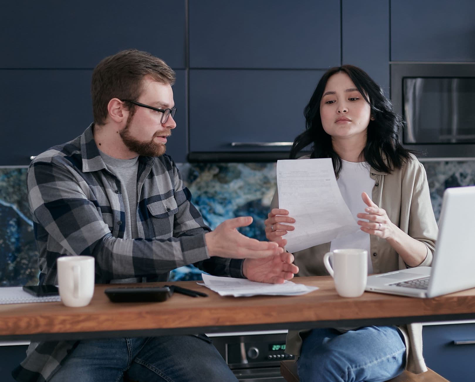 A couple having a discussion over financial documents at home with a laptop.