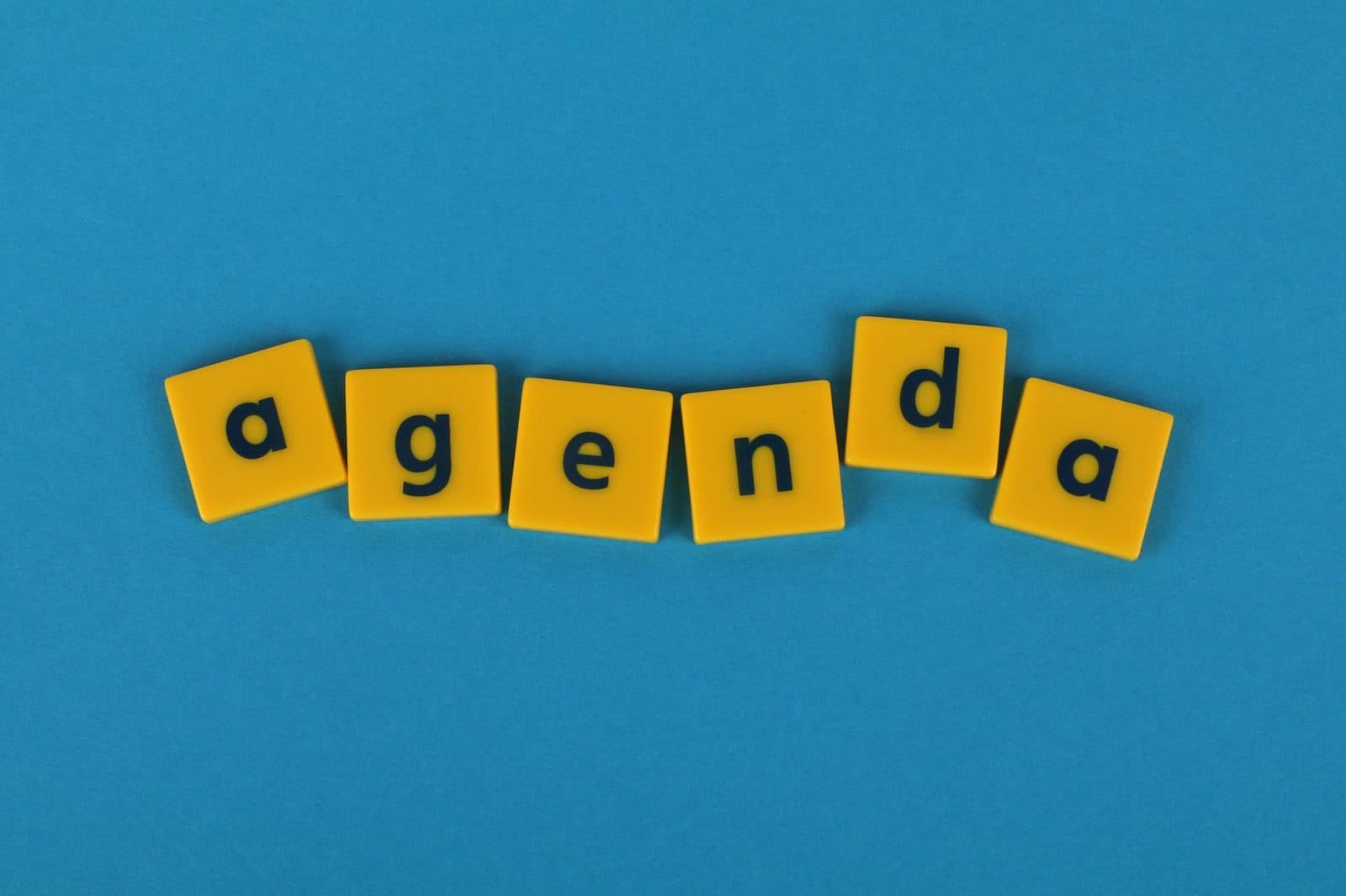 Yellow letter tiles spell 'agenda' on a blue background, symbolizing planning and business.