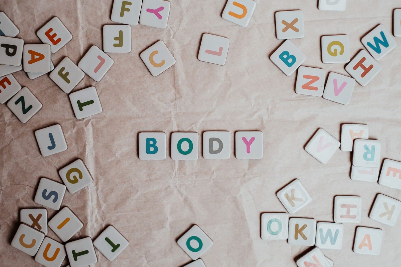 Top view of scattered letter blocks spelling the word 'body' on textured paper.