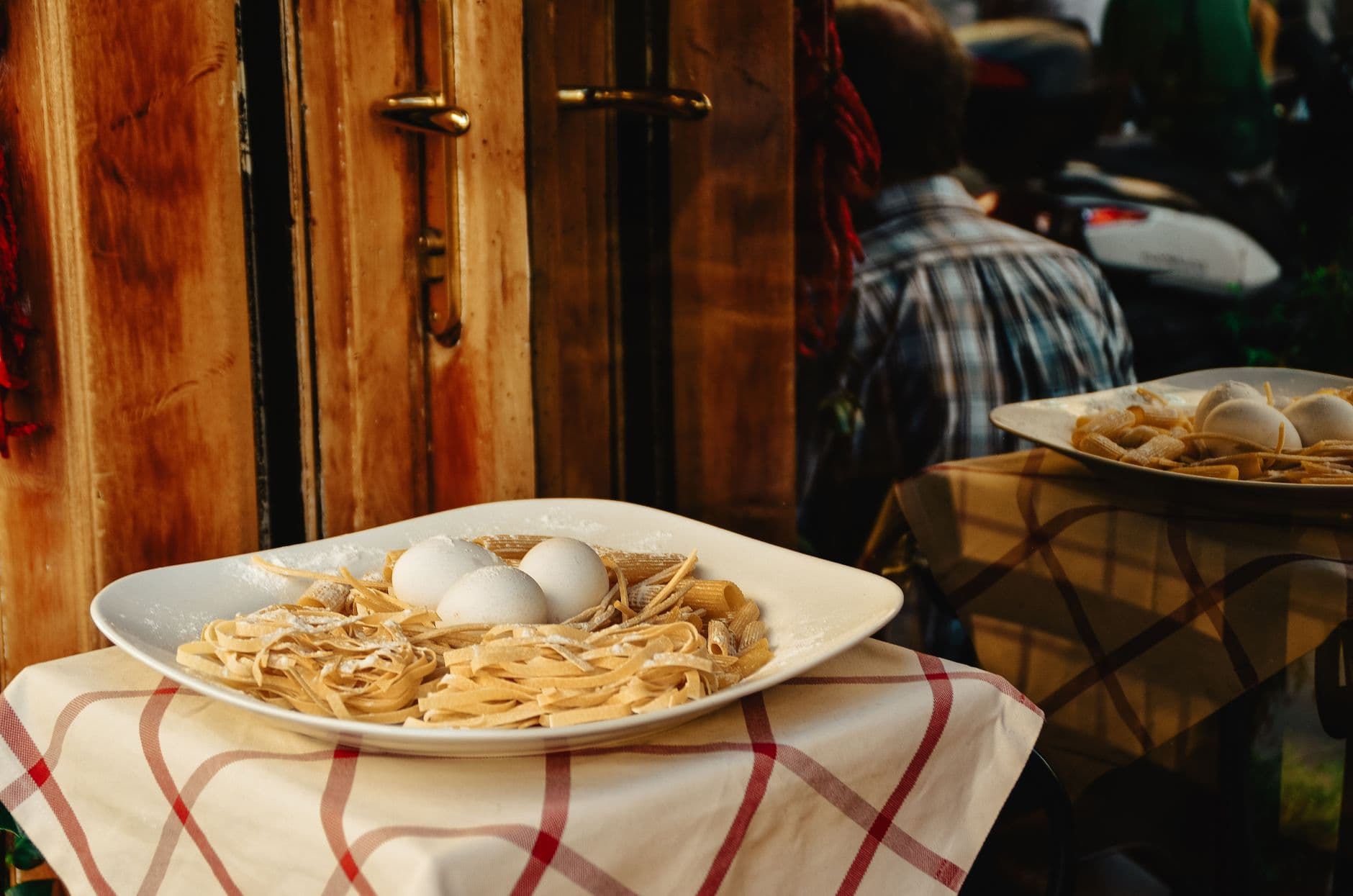 A plate of fresh pasta with eggs is displayed outside a Rome restaurant, showcasing Italian cuisine.