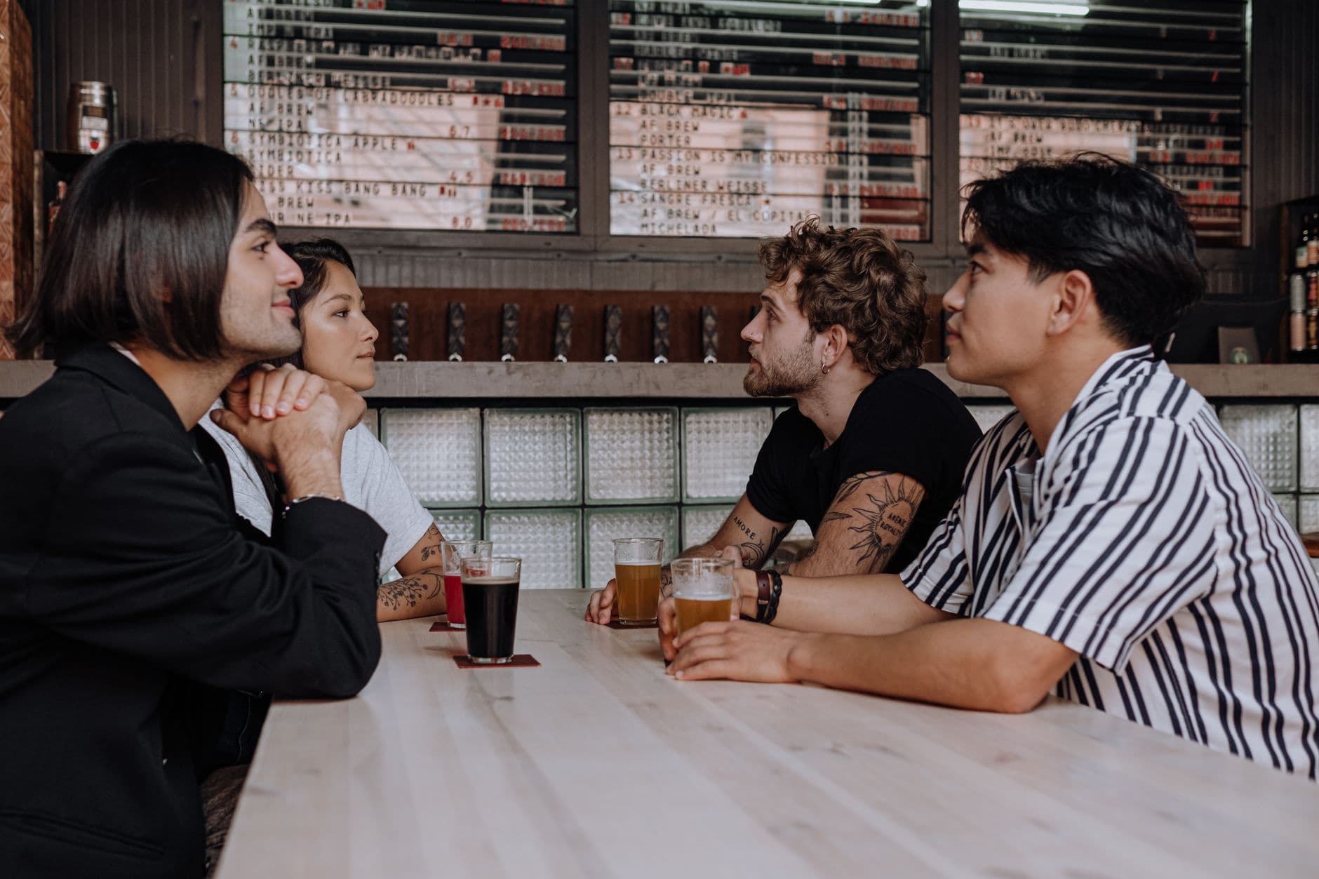 Group of friends sitting at a wooden table in a stylish bar, chatting and enjoying drinks.