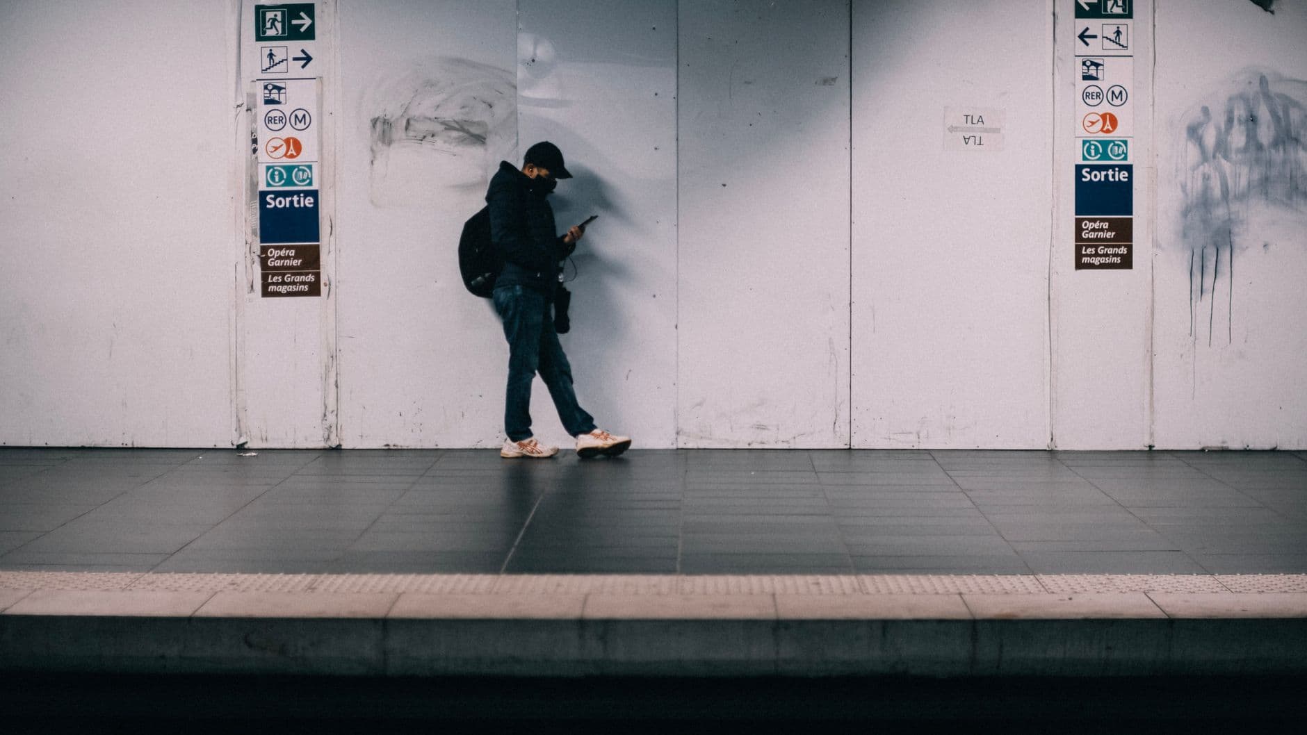 Man wearing a face mask using a phone while waiting in a train station.