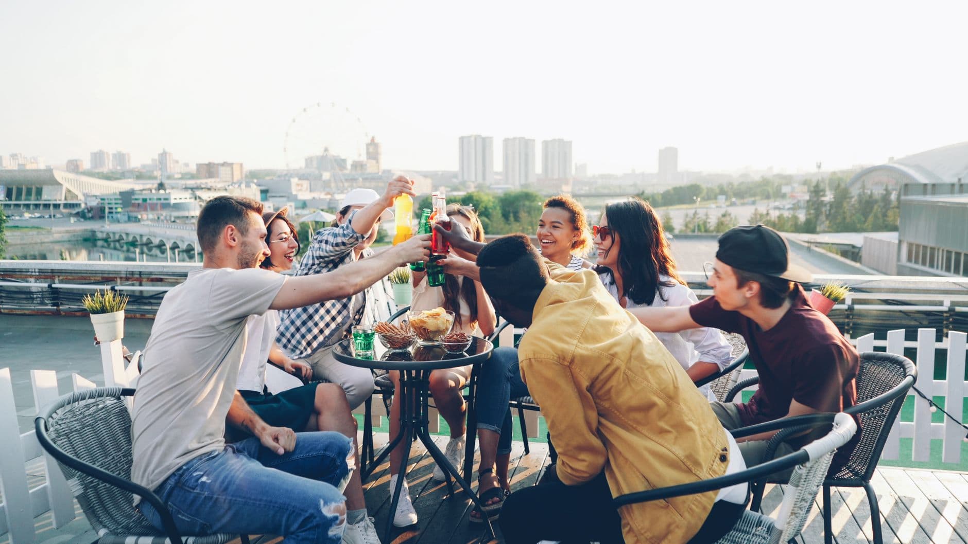 A group of friends toasting with drinks on a scenic rooftop terrace during the day.