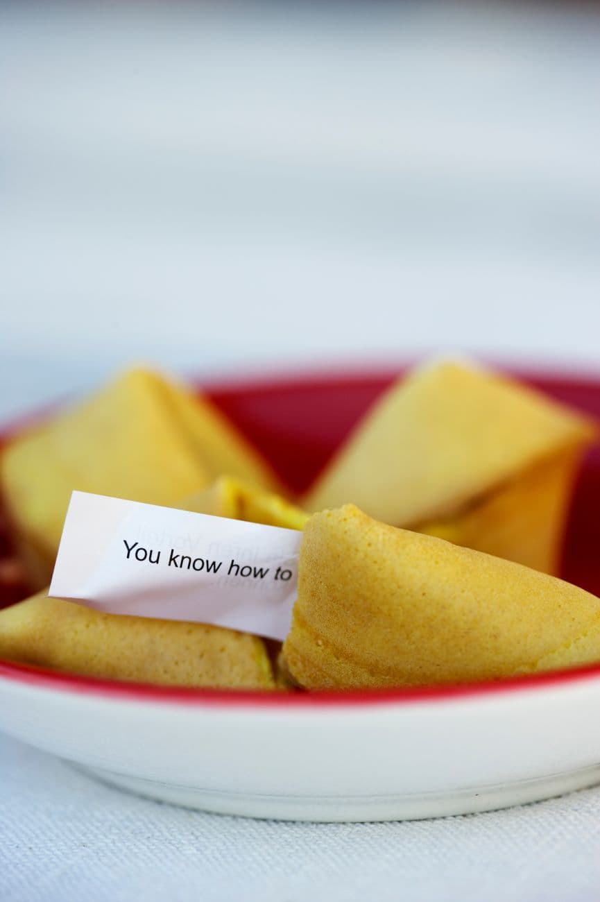 Close-up of a fortune cookie with a positive message, set in a red-rimmed bowl.