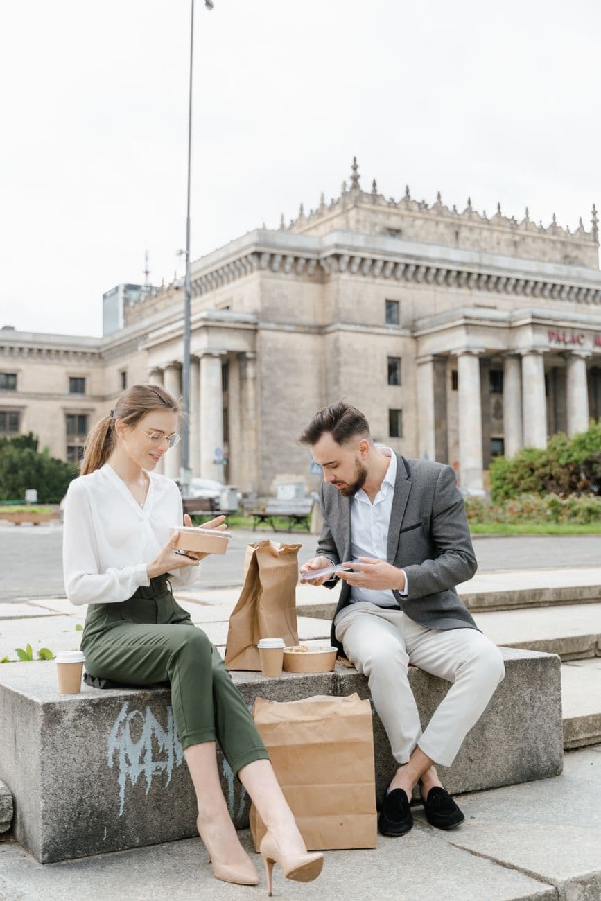 Two business professionals sitting outside enjoying takeout lunch together.