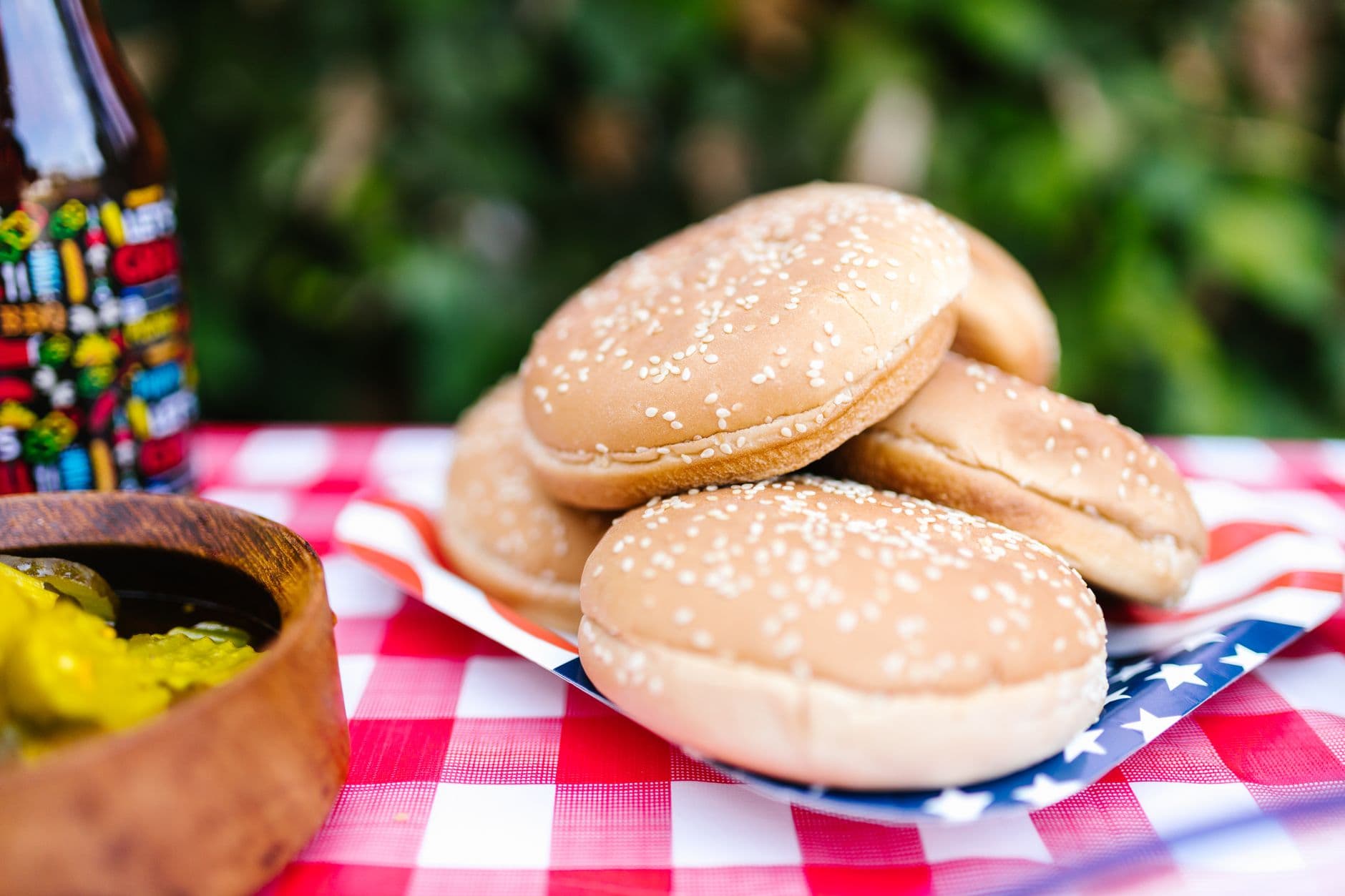 Stack of sesame seed hamburger buns on a checkered tablecloth ready for a summer BBQ.