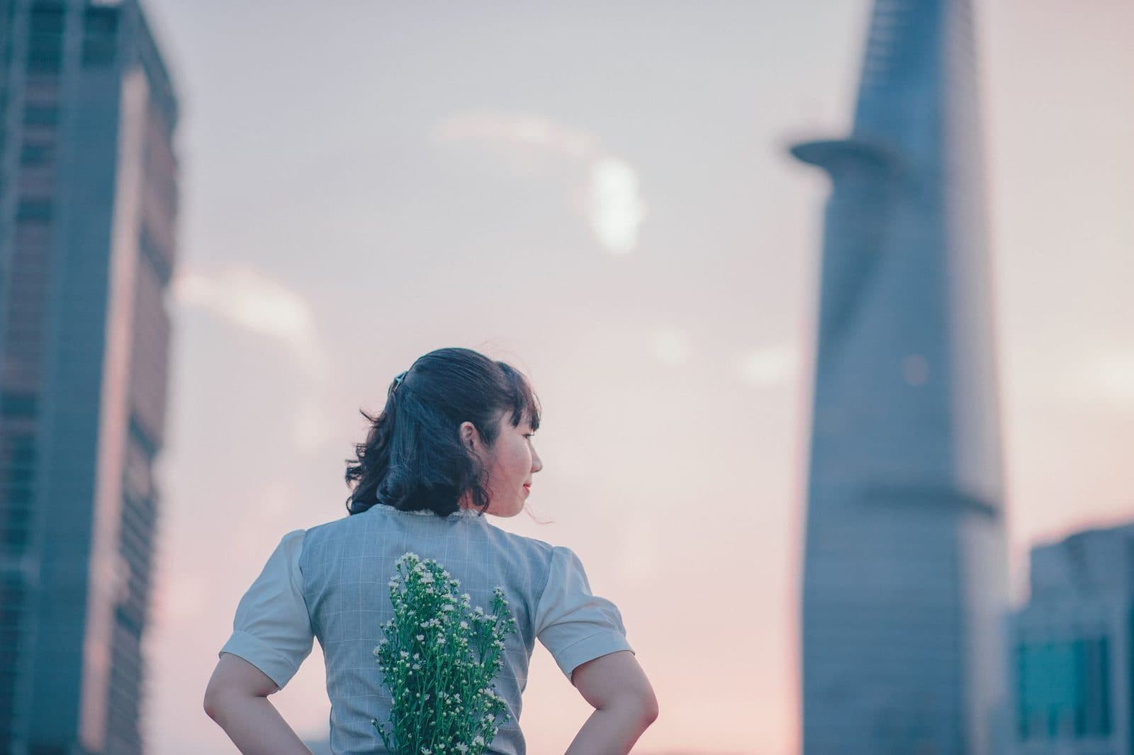 Woman with flowers in a cityscape at sunset, blending nature with modern architecture.