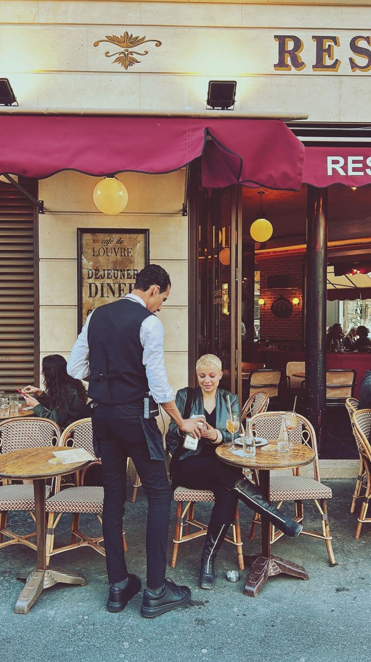 A waiter serves a woman at a Parisian cafe. Classic street life in Paris, France.