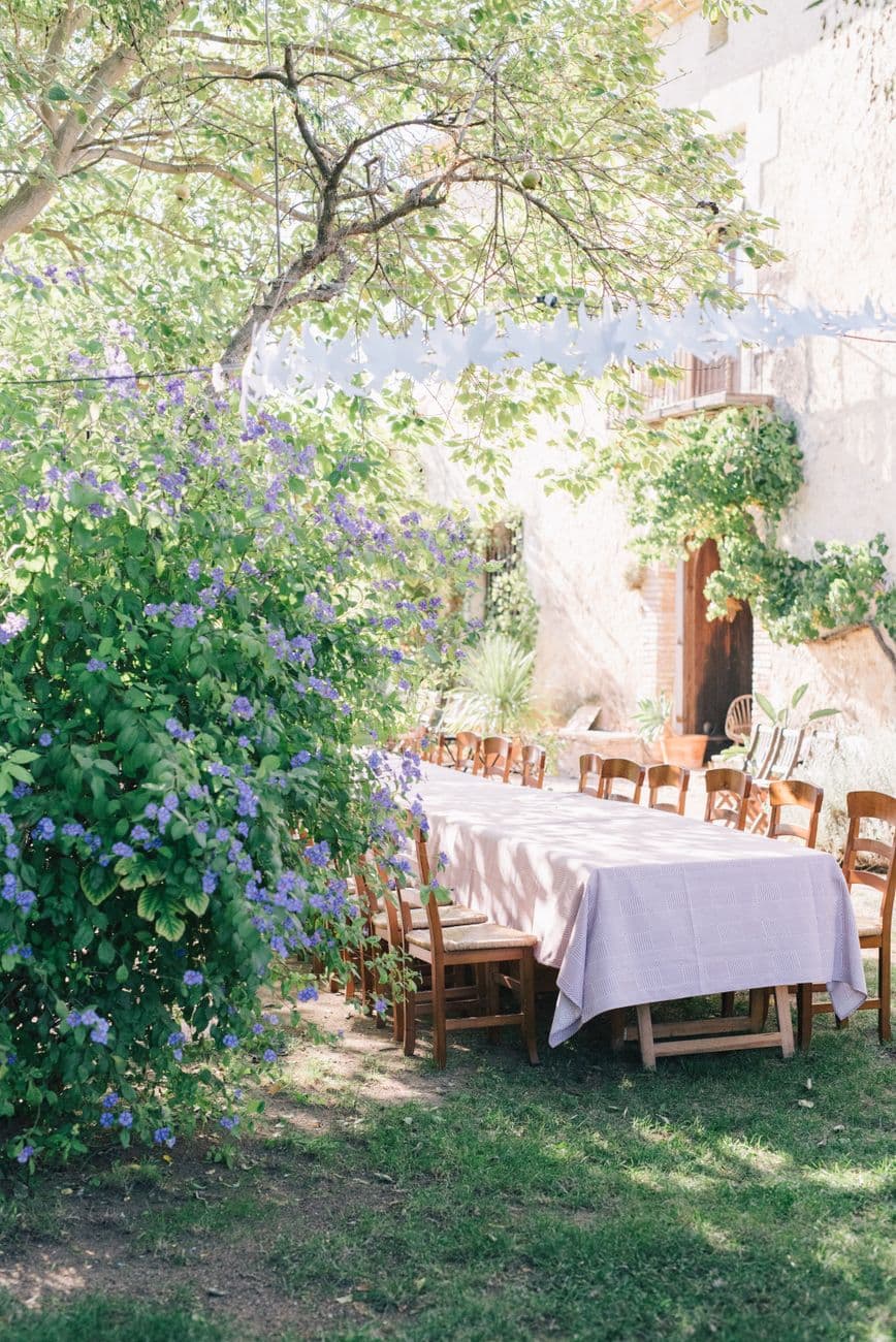 A beautiful outdoor dining area set amidst lush greenery with wooden chairs and a table covered in a light tablecloth.