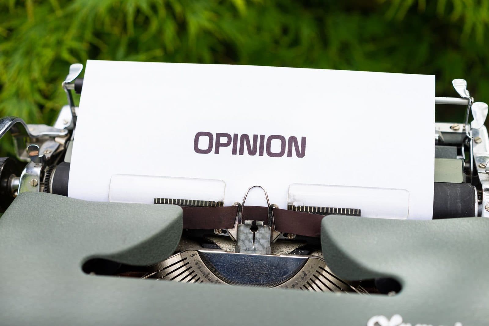 Close-up of a typewriter with paper showing the word 'Opinion' outdoors.