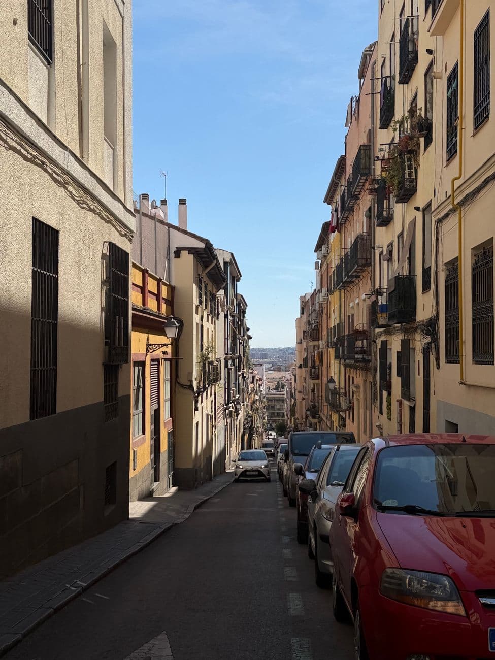 Charming narrow city street in Madrid lined with parked cars and traditional buildings.