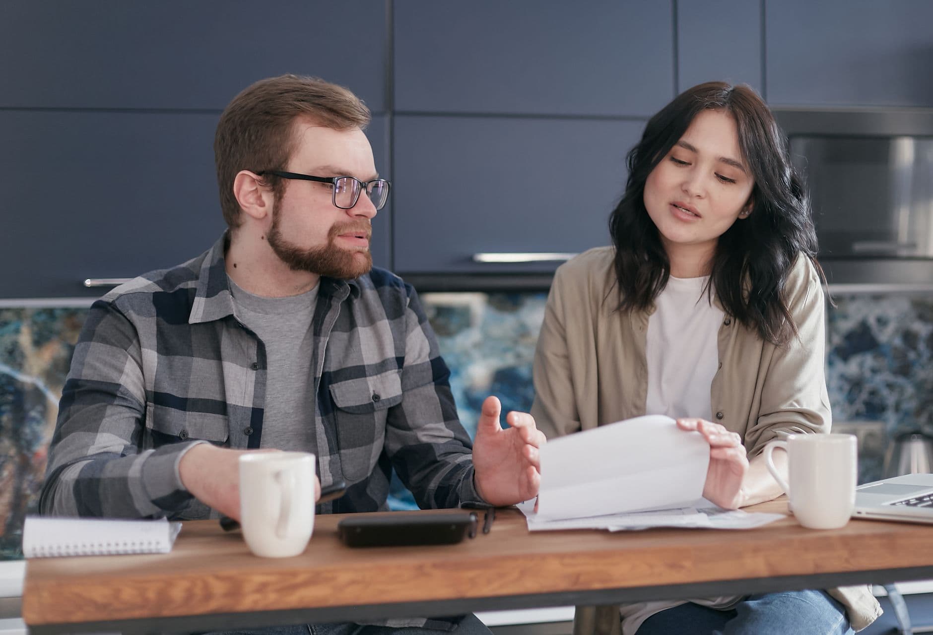 Two colleagues having a discussion during a casual team meeting with coffee and documents.