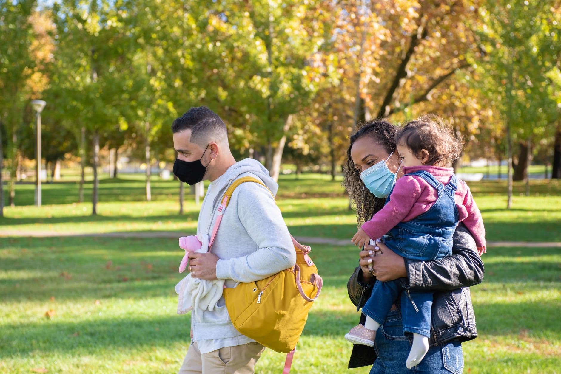 A family enjoying a walk in the park during autumn, wearing masks for safety.