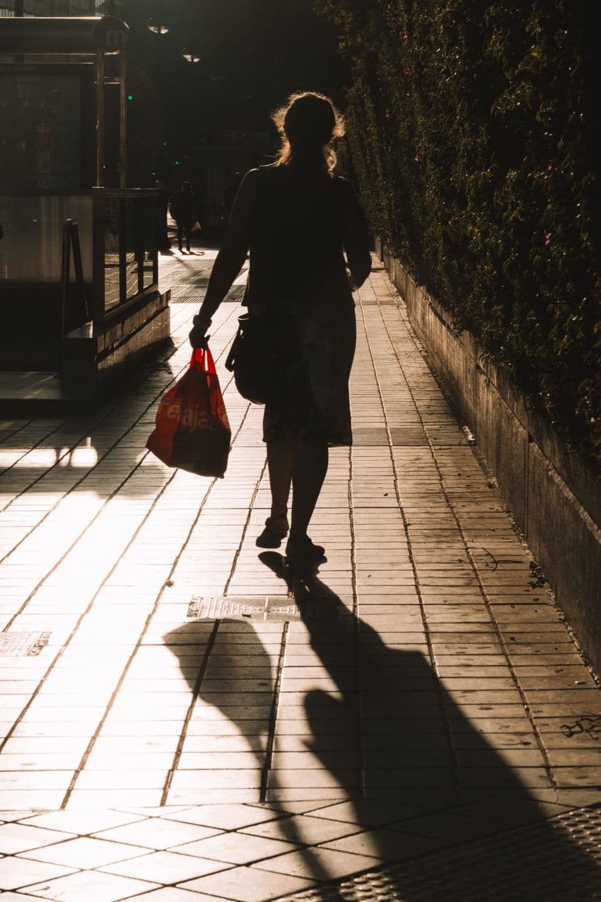 Silhouetted woman walks on sunlit sidewalk casting long shadows in urban setting.