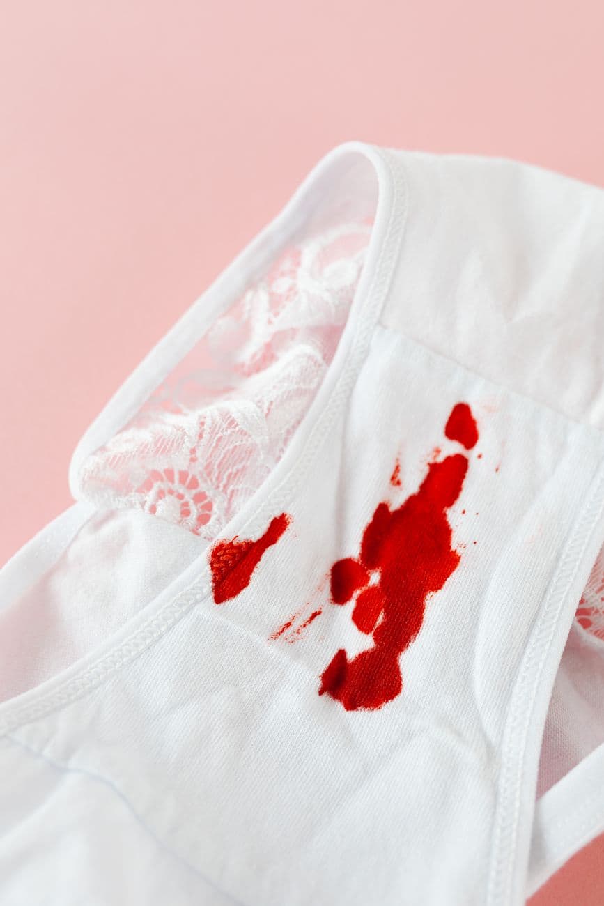 White underwear with menstrual blood stains on a pink background, symbolizing menstruation.