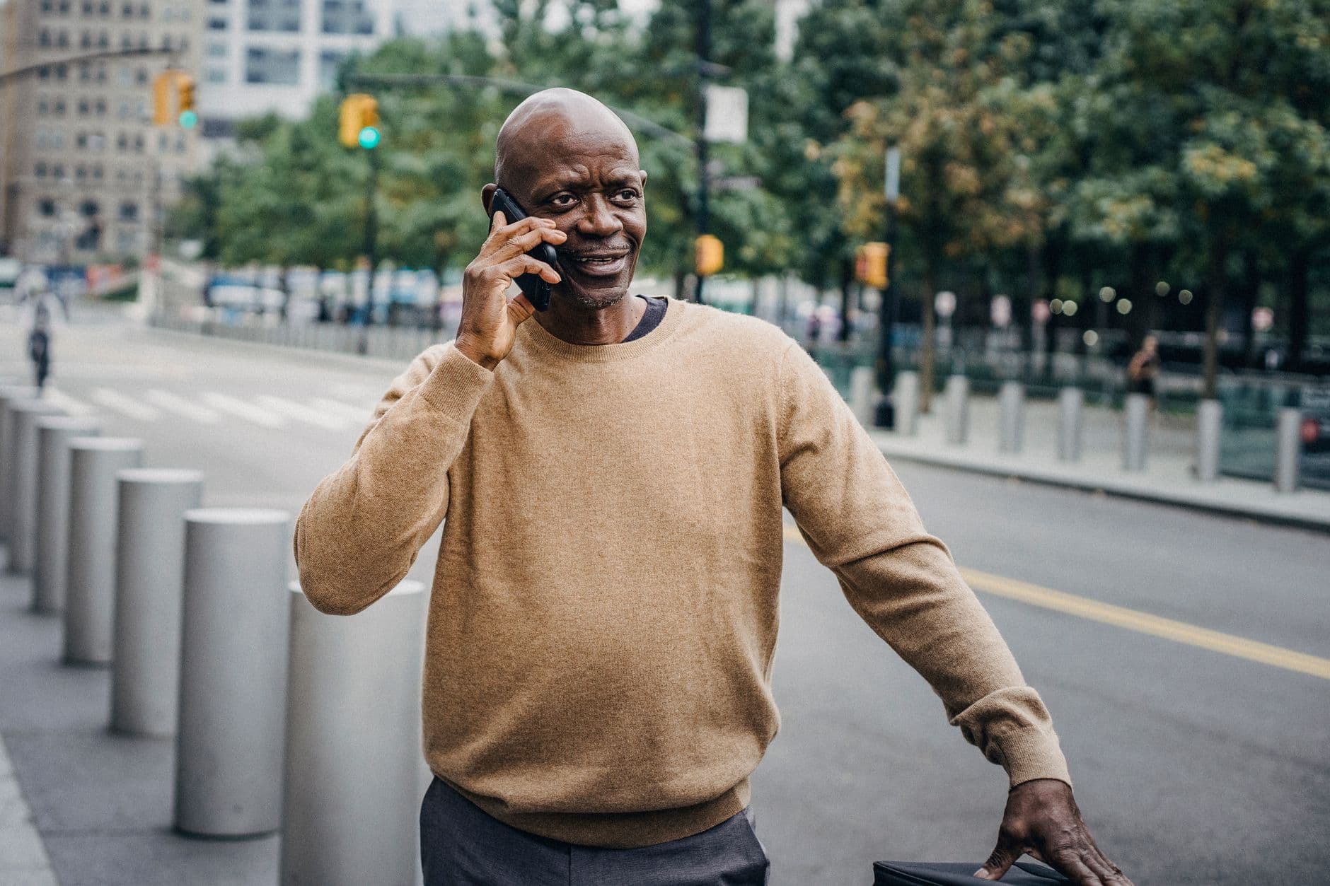 Focused African American middle aged male talking on smartphone while standing on roadside with cement pillars on street while looking away