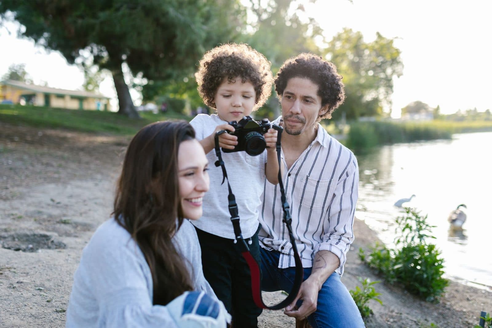 A joyful family moment by the lake as a child captures memories with a camera.
