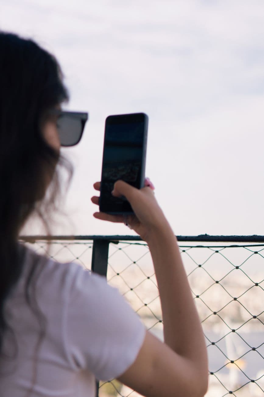 A woman in sunglasses takes a photo with her smartphone, capturing city views in Istanbul, Türkiye.
