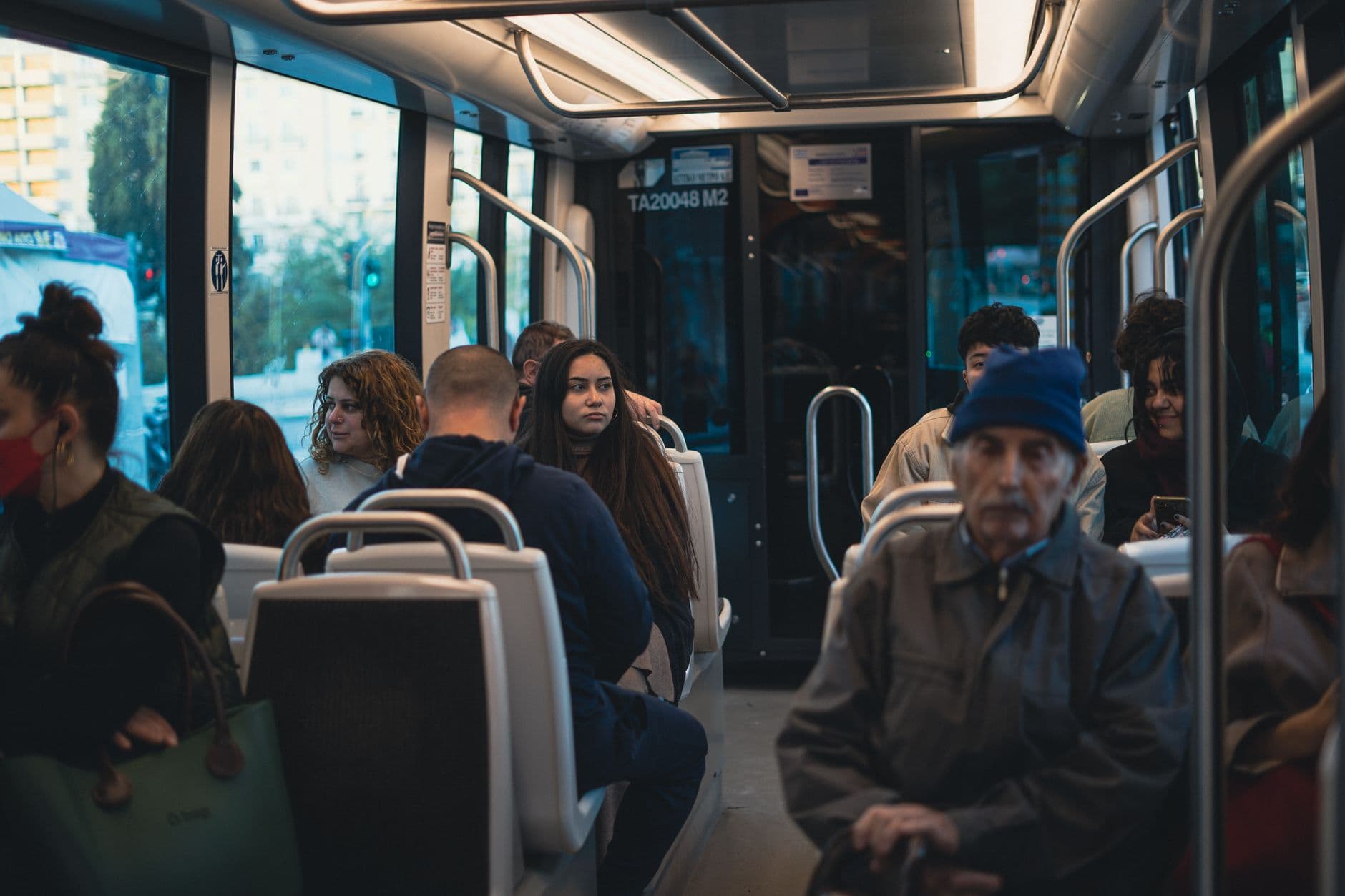 Passengers of various ages engaged in activities on a crowded urban bus during the day.