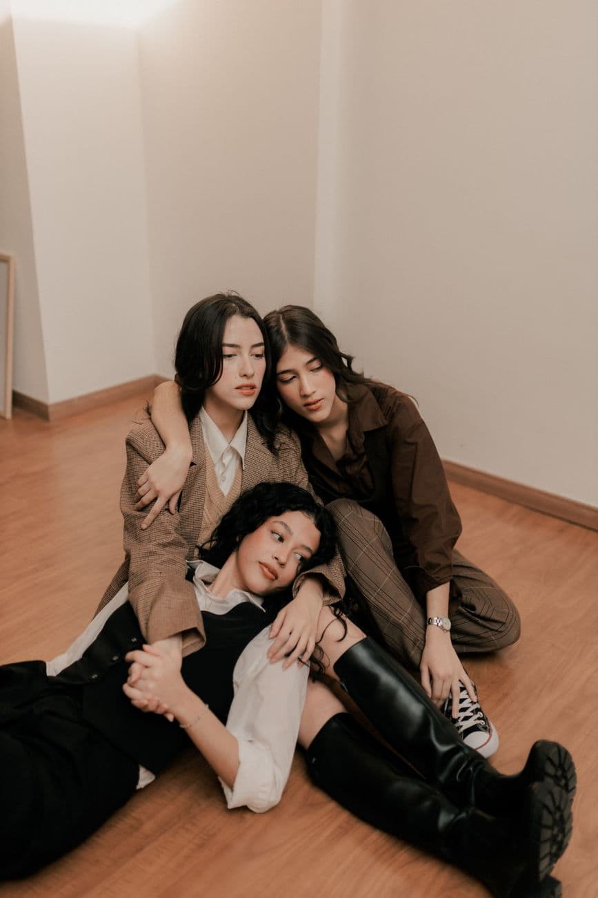 Close-up of three young adults sitting on a wooden floor indoors, showing friendship and togetherness.
