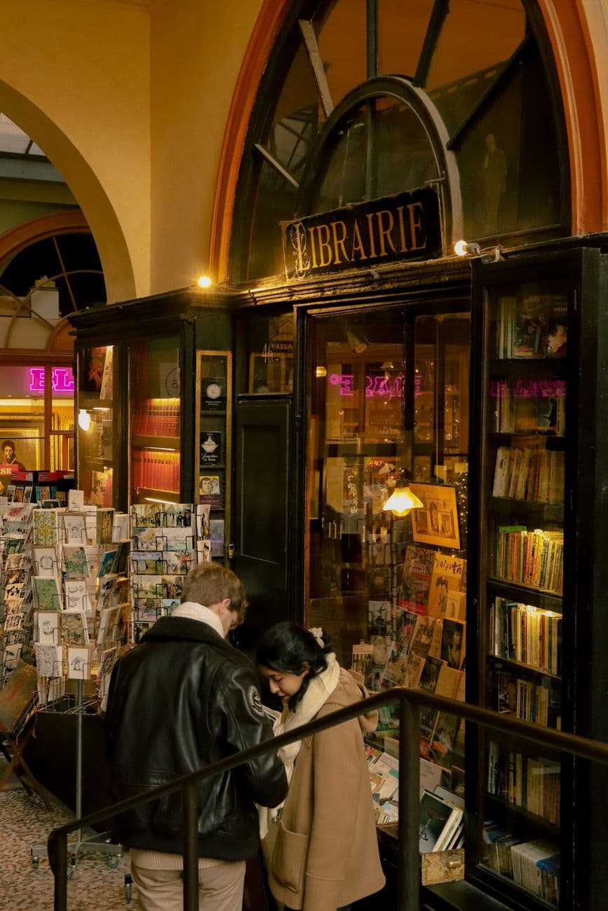 Customers browsing outside a charming Parisian bookstore in an indoor market setting.