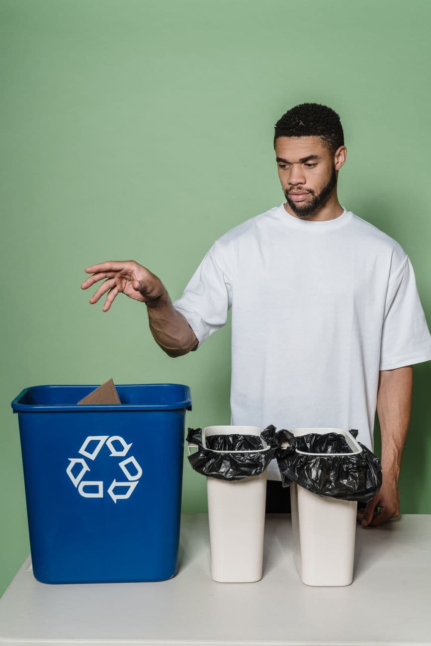 Man in white shirt recycling in studio with blue bin and green background.