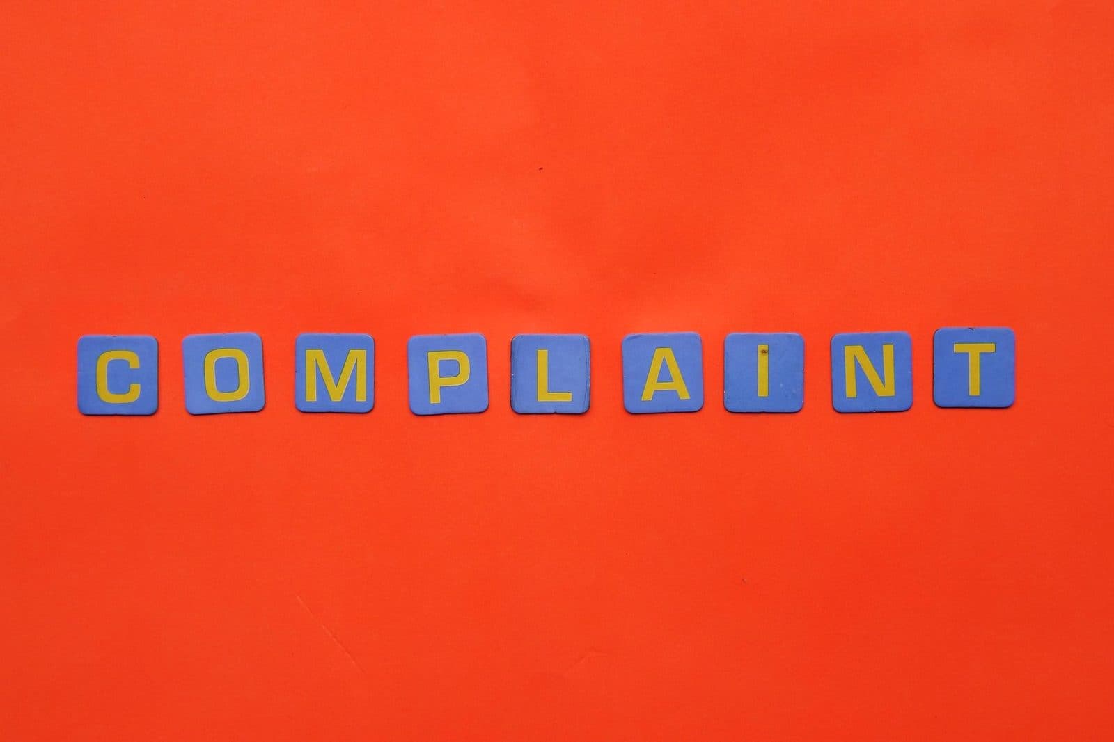 Blue letter tiles spelling 'COMPLAINT' on a vibrant red surface.