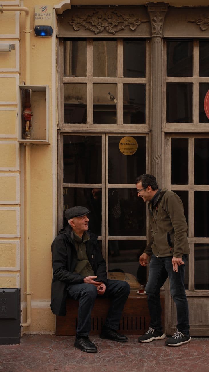 Two men chatting in front of a vintage building on a city street.