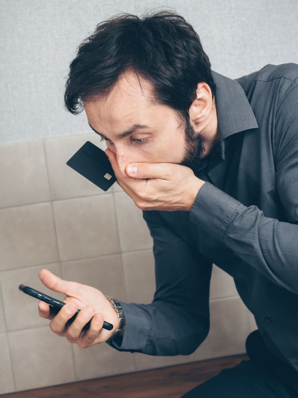Man in shock discovering possible fraud or data breach with smartphone and credit card.