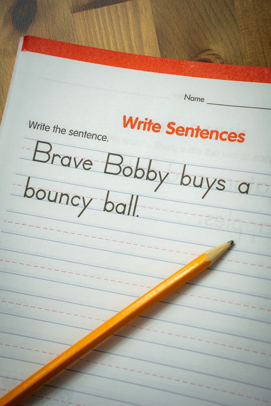 Writing sentence practice with a pencil on a lined workbook for elementary students.