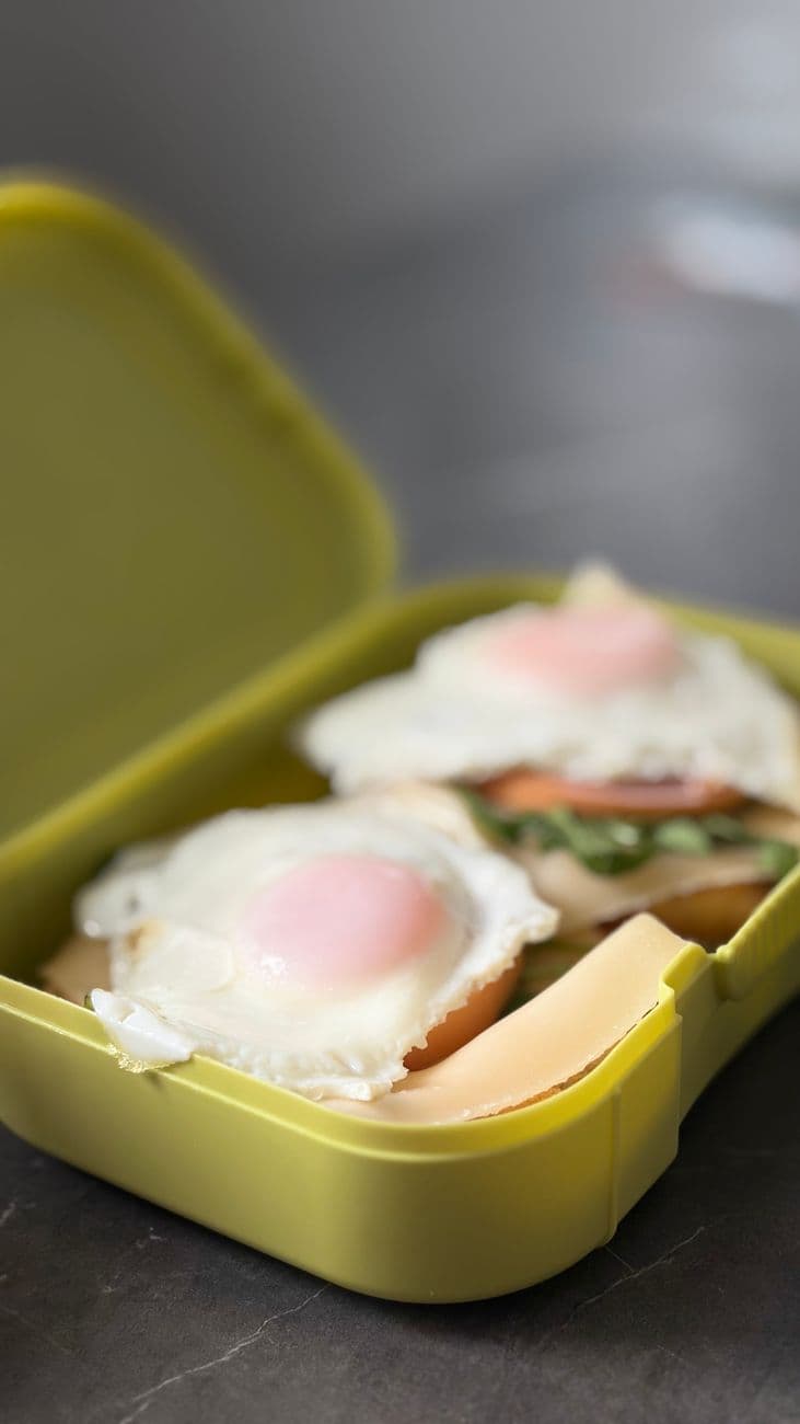 Delicious breakfast sandwiches with eggs in a bright yellow lunch box on a table.