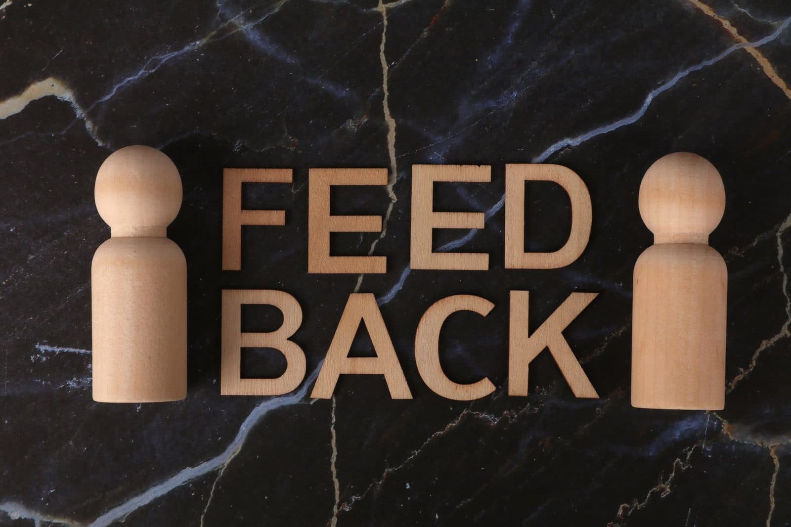Wooden letters spelling 'Feedback' with peg-like figures on marble background.