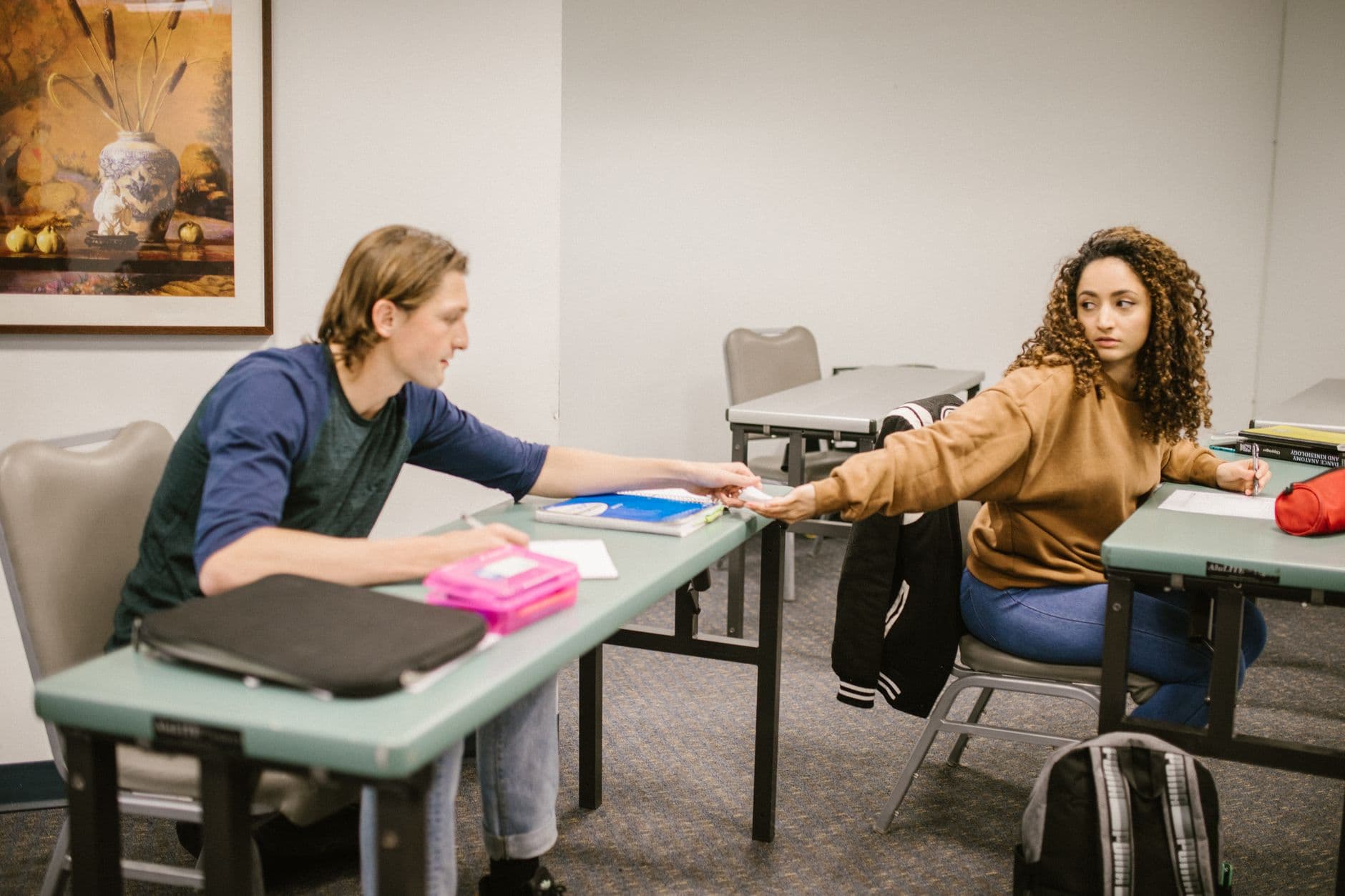 Two college students exchanging papers in a classroom setting, emphasizing interaction and study.