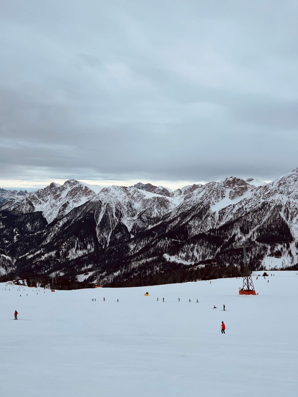 A serene winter landscape featuring skiers on a snowy slope in the Italian Alps.