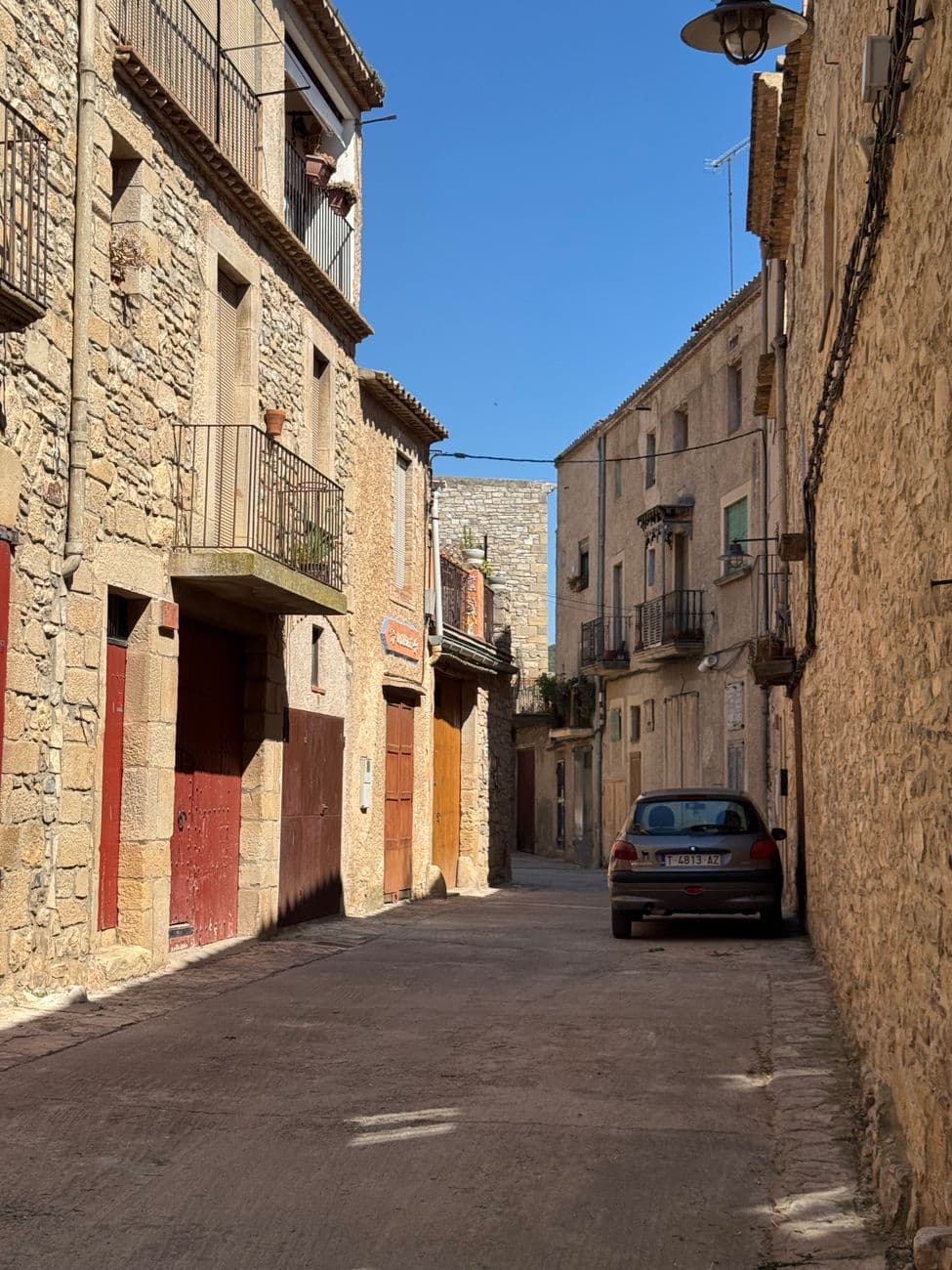 Picturesque narrow street in medieval Guimerà, Spain, with stone buildings and a clear blue sky.