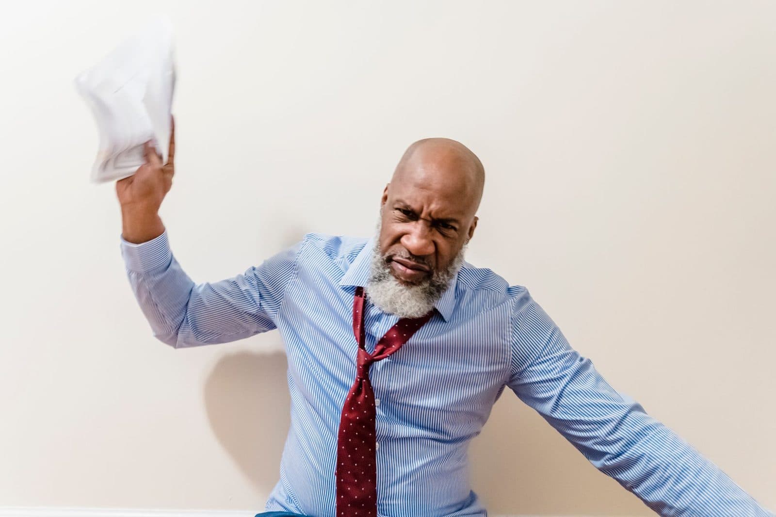 A bald man in a blue shirt expresses anger by throwing papers indoors.