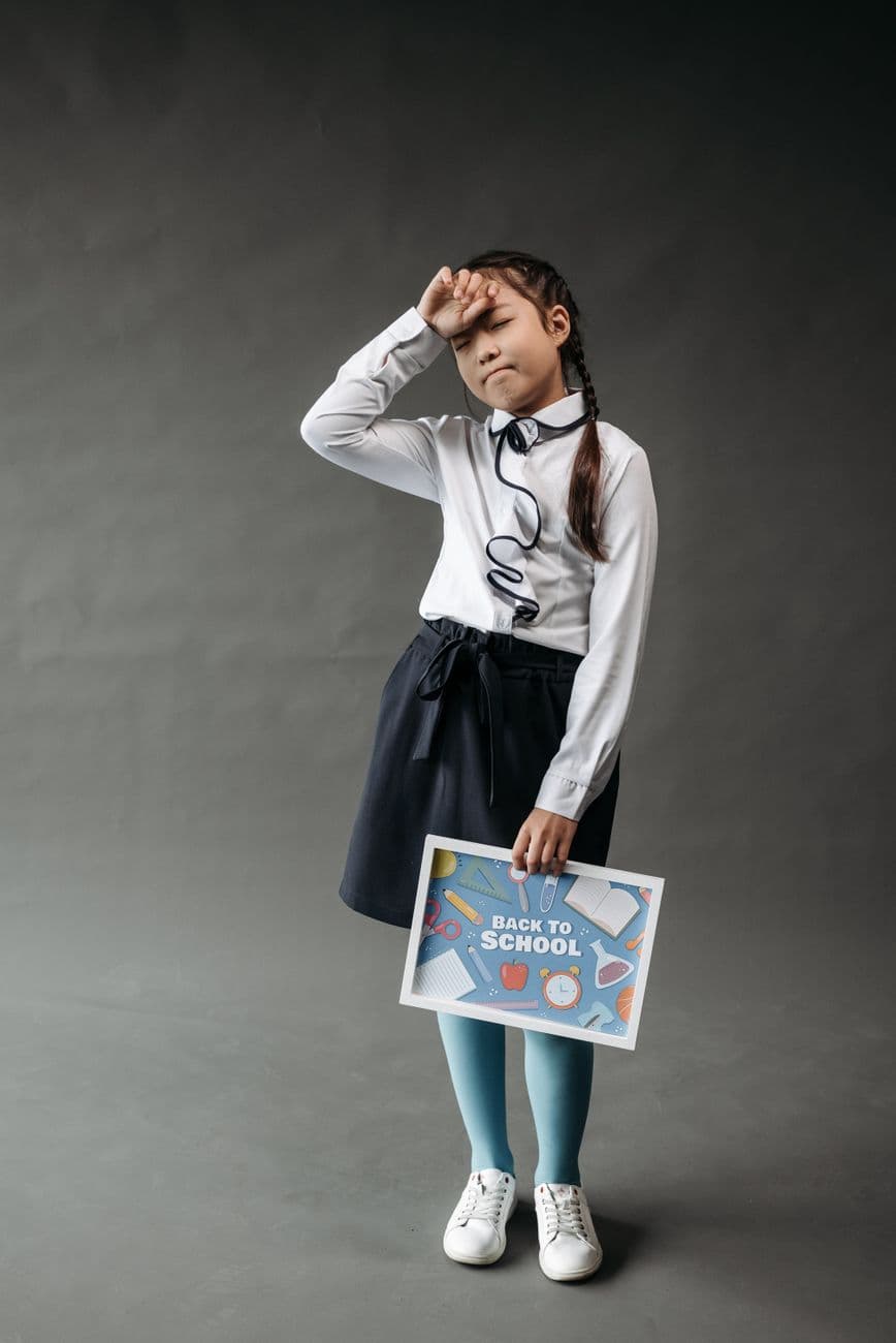 A young girl in uniform holding a 'Back to School' sign, expressing contemplation.