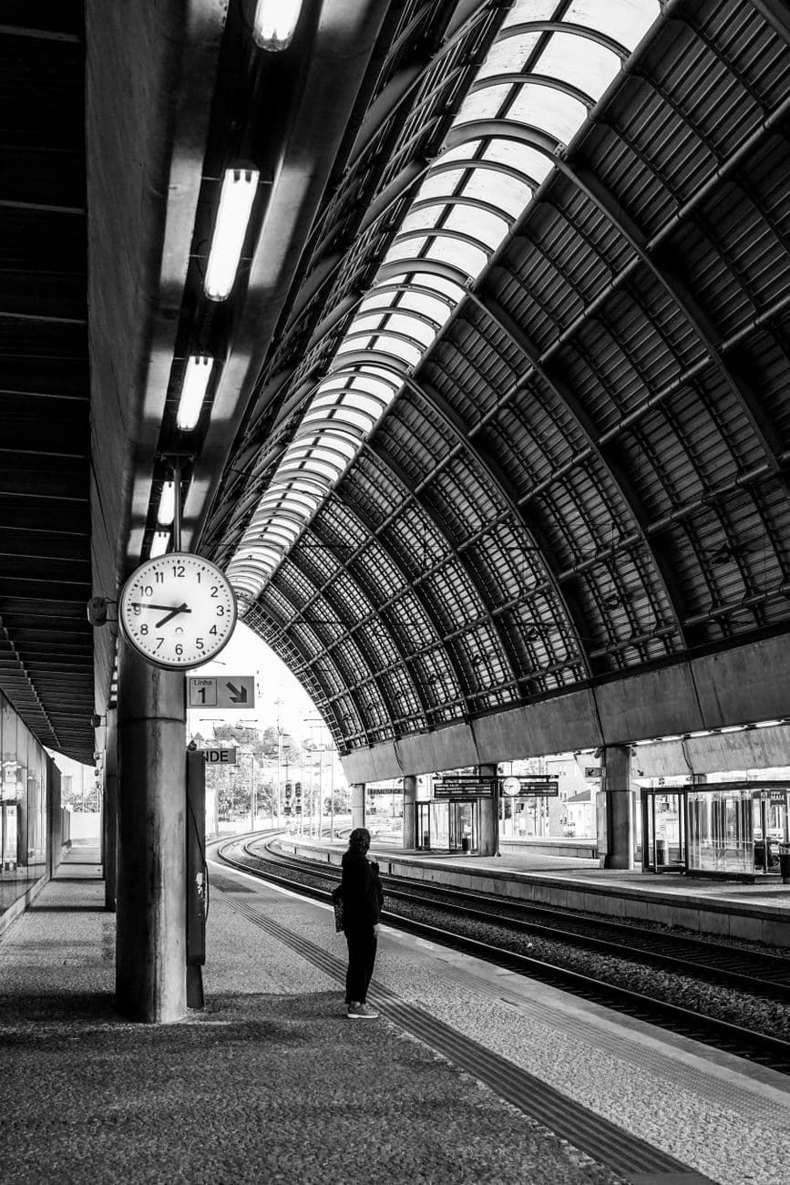 Black and white photo of a woman standing on a city railway platform.