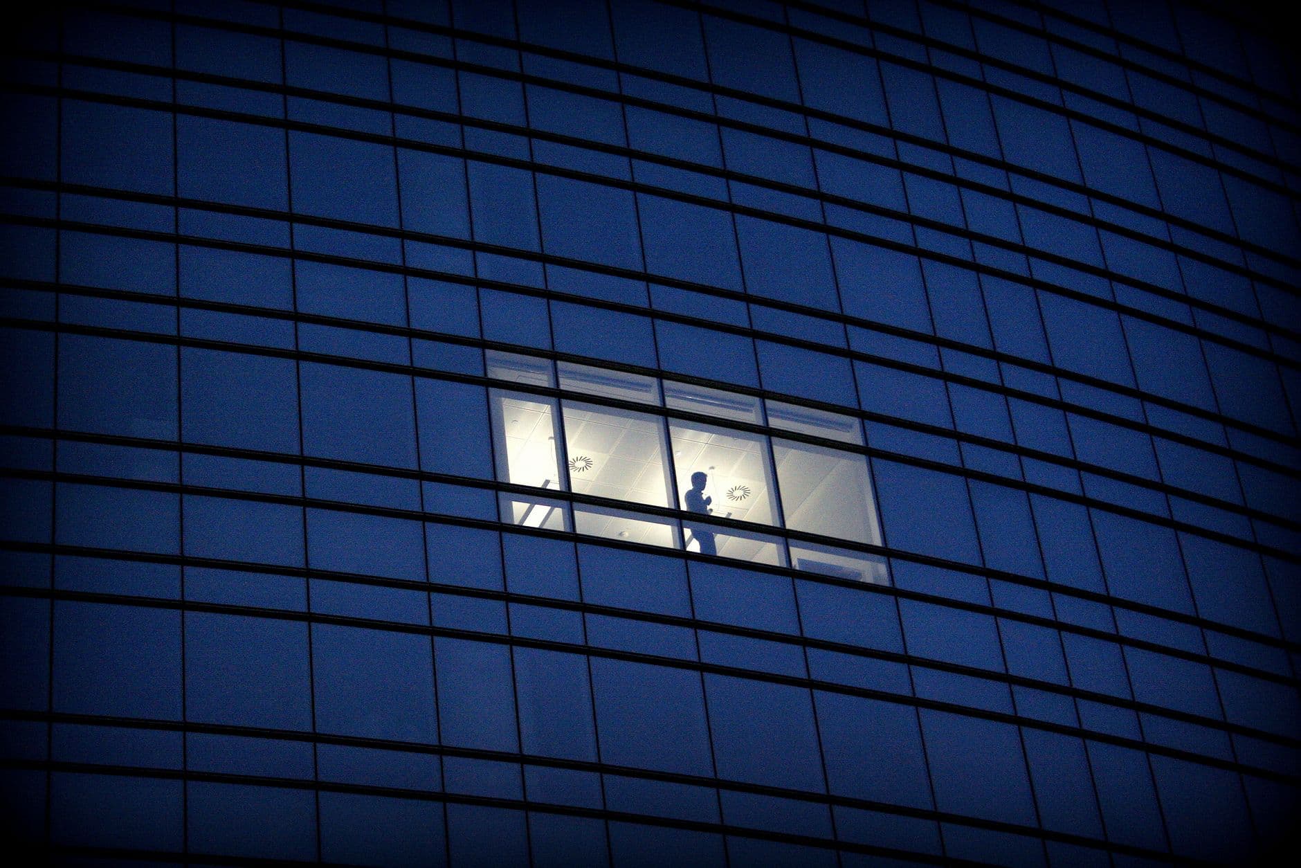 Silhouette of a man working late in a modern glass building, showcasing architecture and solitude.