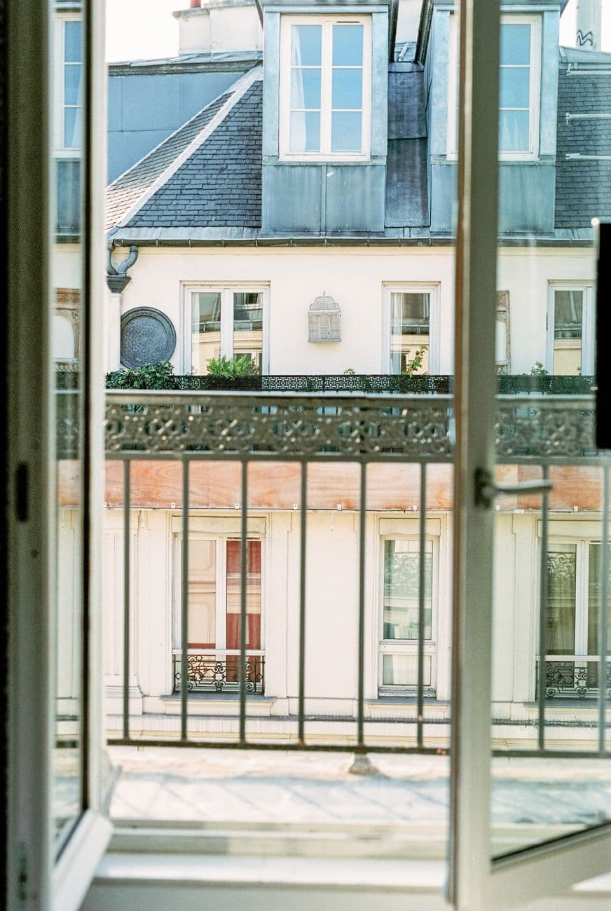 Charming view of Parisian architecture through an open window showcasing classic French balconies.