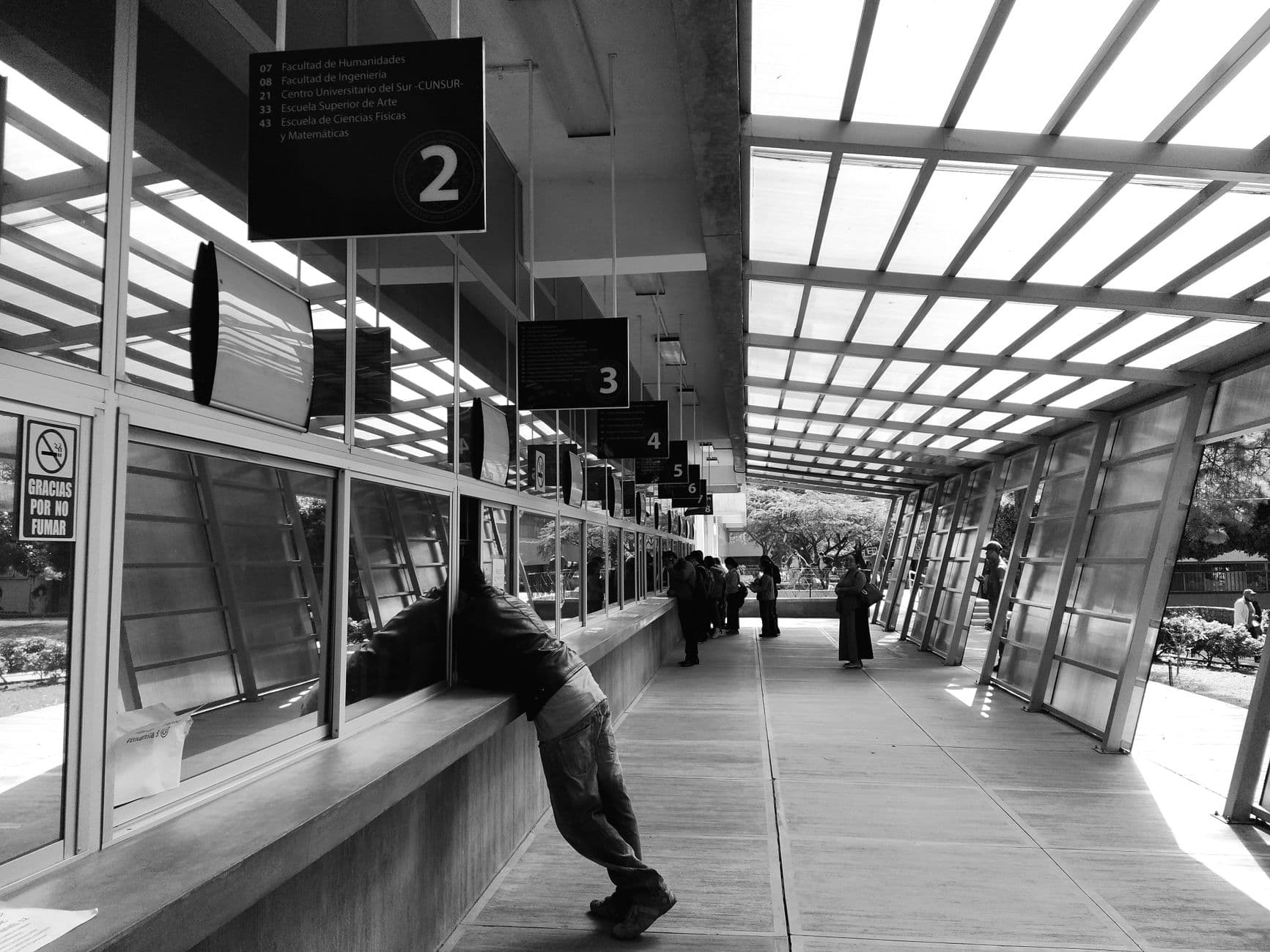 People queuing indoors at a service counter in Ciudad de Guatemala captured in black and white.
