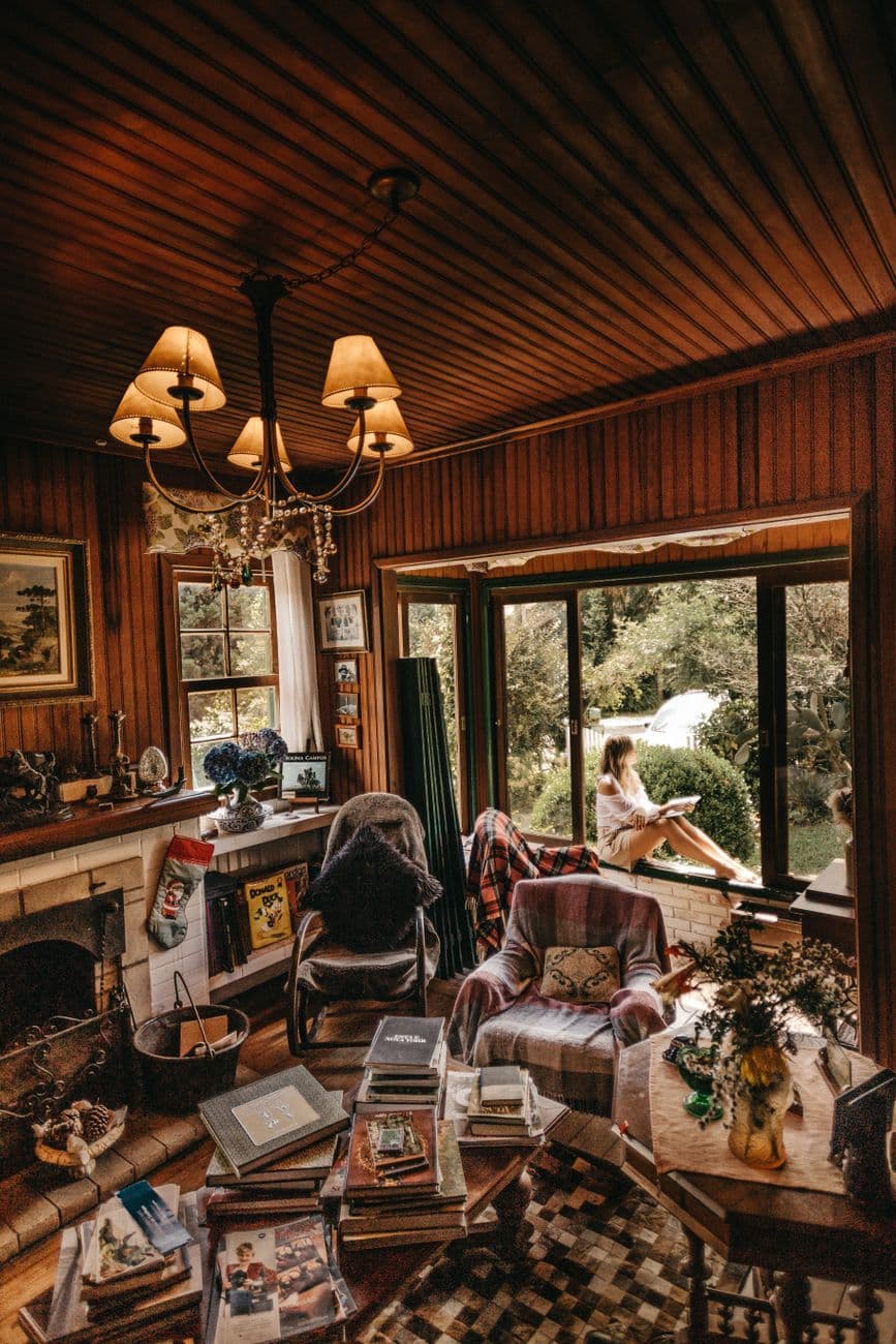 Warm rustic living room featuring vintage decor and a scenic window view with a woman enjoying the outdoors.