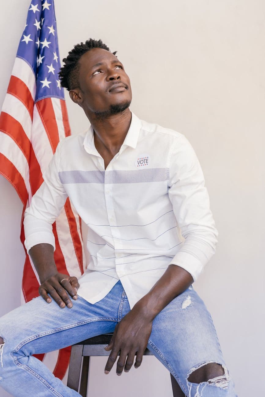 A man seated in a studio with an American flag, representing patriotism.