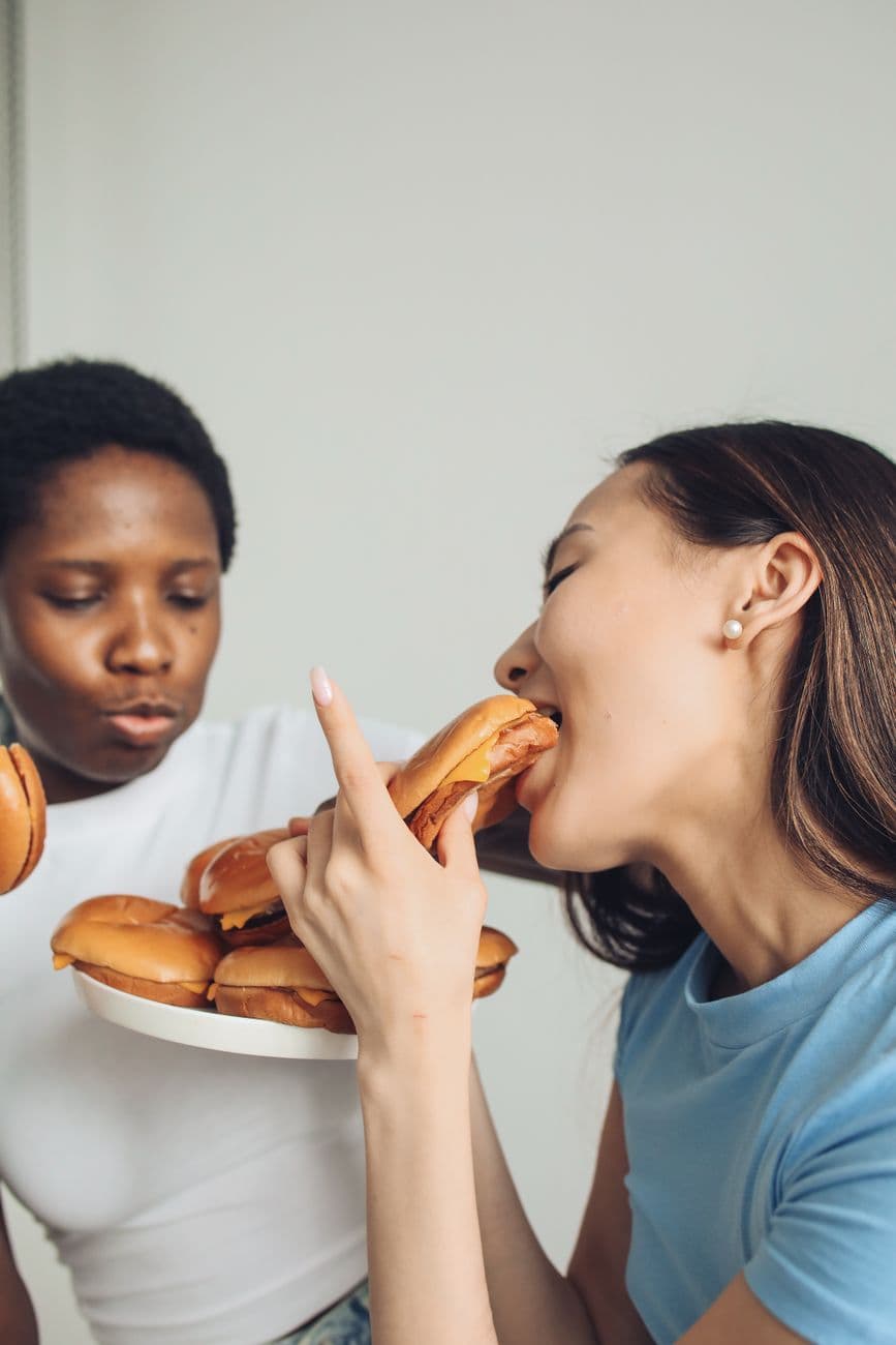 Happy women indulging in delicious burgers indoors.