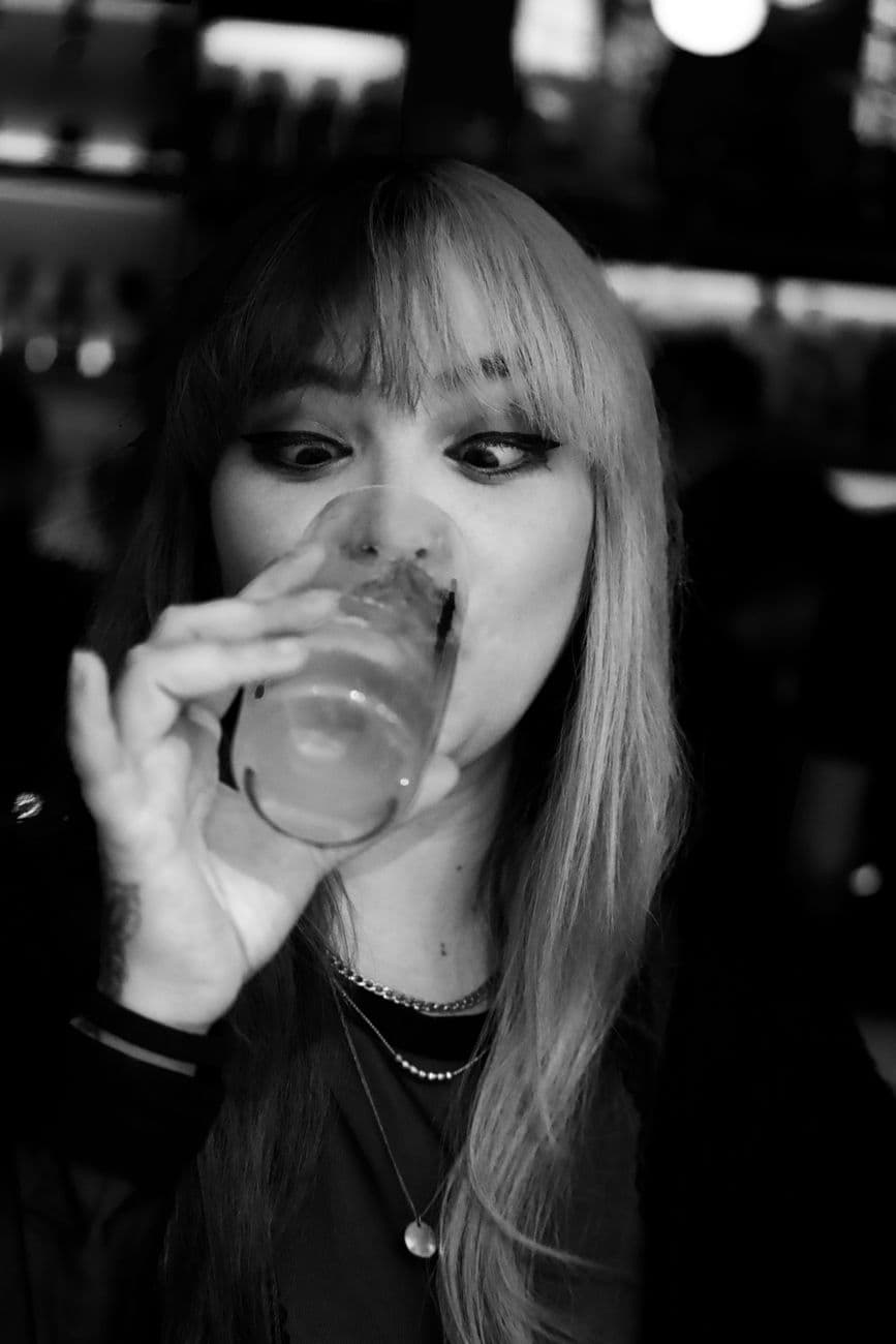 A woman enjoys a cocktail in a cozy bar, captured in black and white.