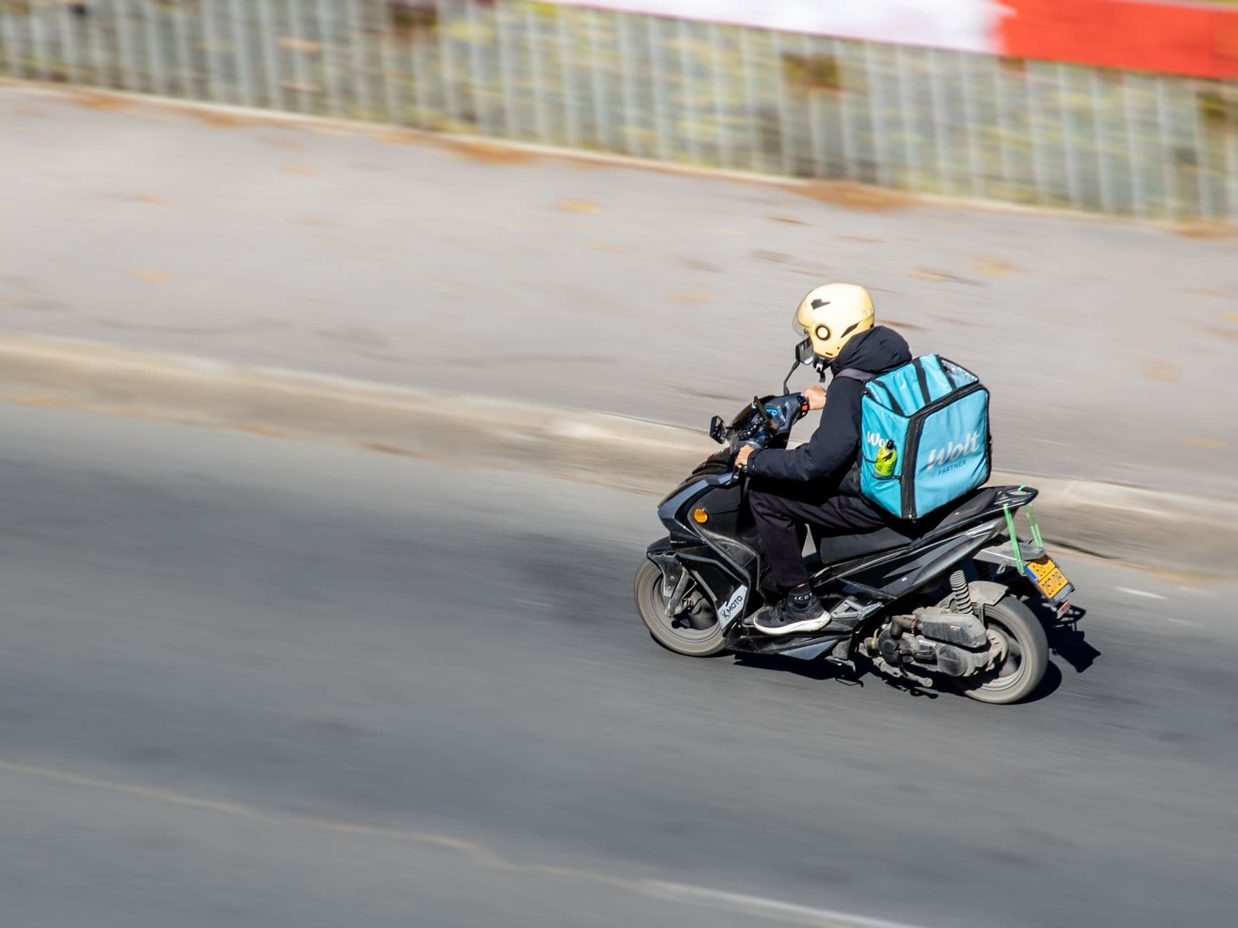 A food delivery person riding a scooter on a city street, viewed from above.