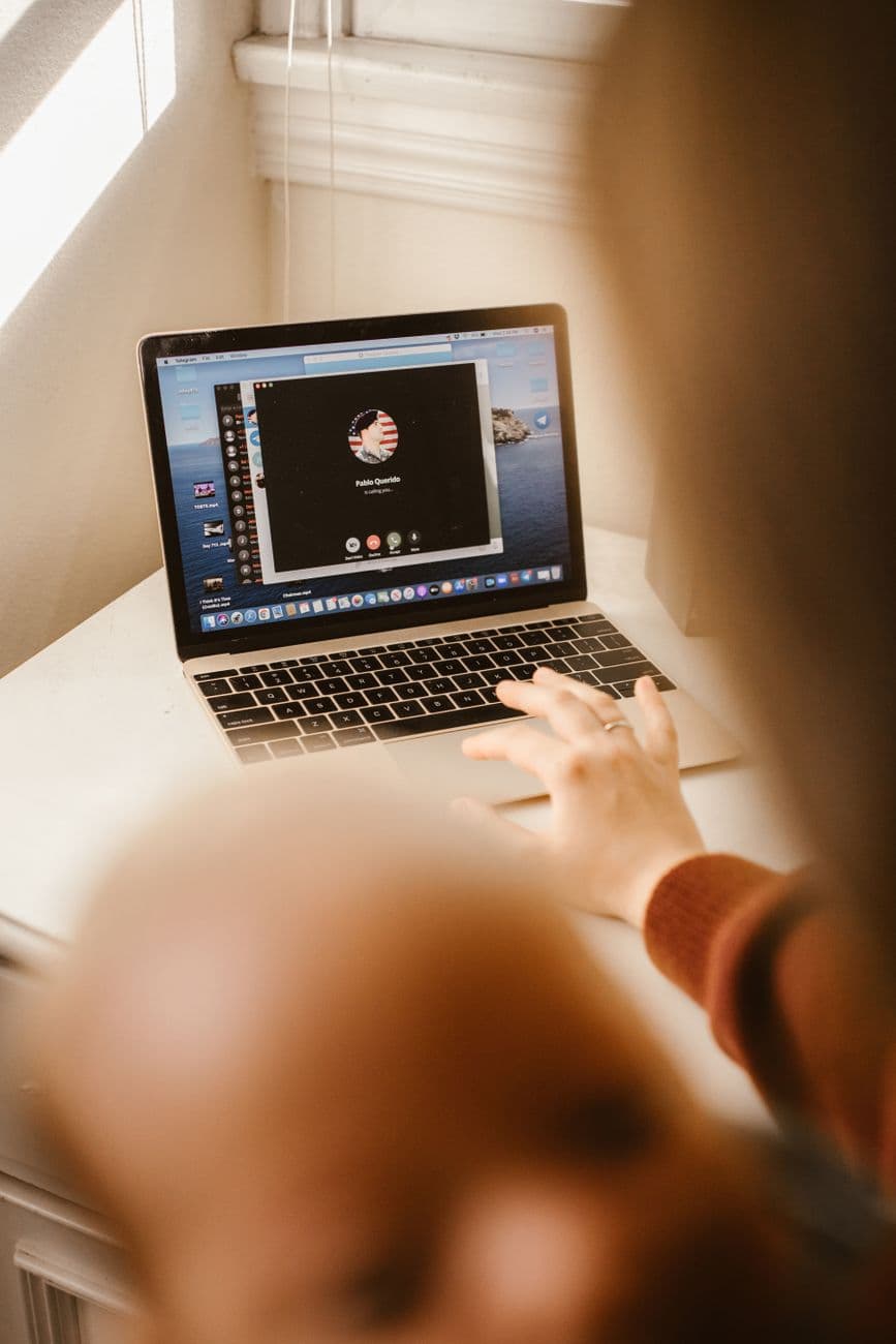 An adult uses a laptop for a video call indoors, focusing on the screen.