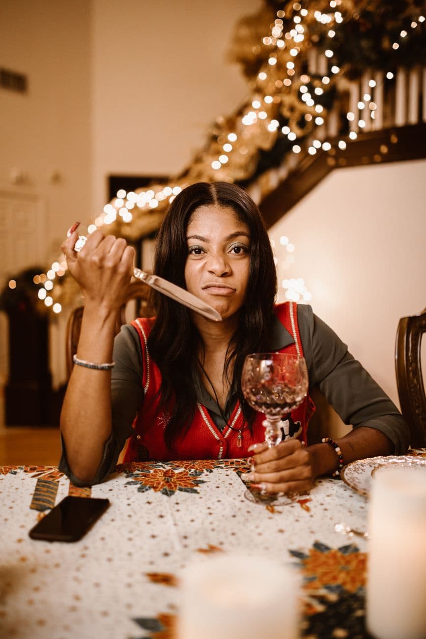 Woman at a festive dinner table with holiday decor, holding knife and wine glass.