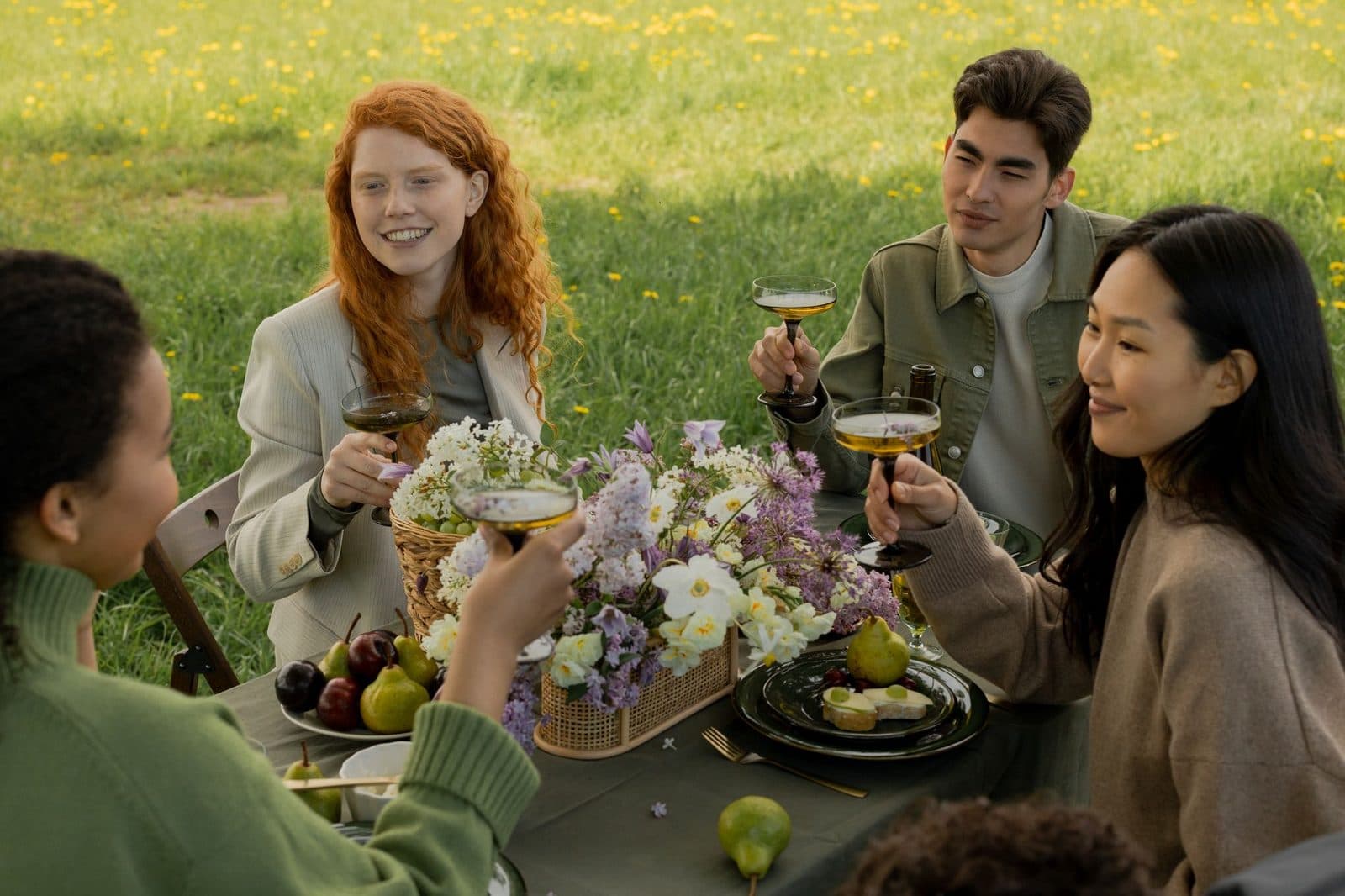 A diverse group of friends enjoying a picnic with wine in a sunny meadow.